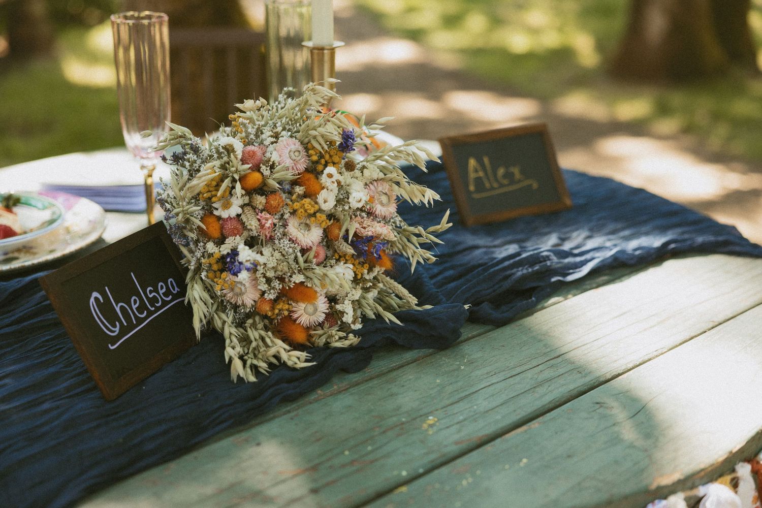 Rustic wedding reception details with dried floral arrangements and slate place cards on a wooden table in natural light.