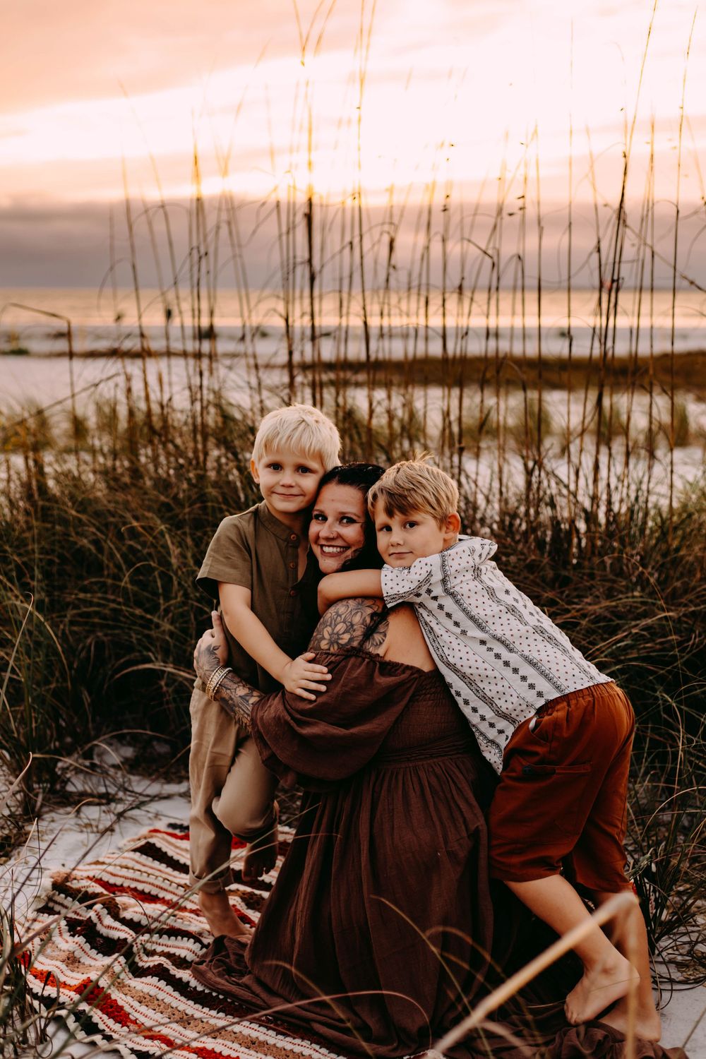 Family enjoying a tender moment together on a blanket at the beach during sunset.