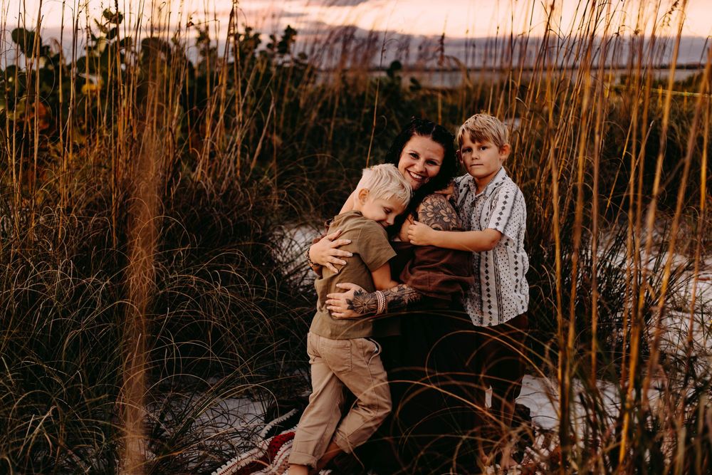 A couple embraces lovingly among tall grass at sunset during a romantic outdoor photo session.
