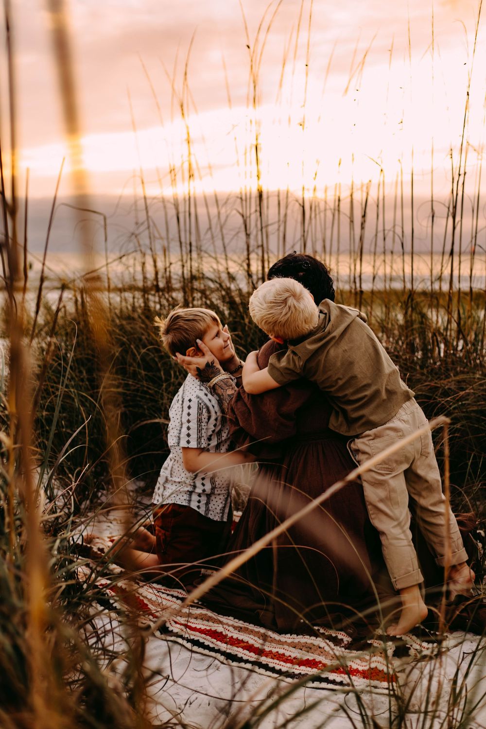 A couple shares an intimate moment on a blanket in tall grass during golden hour sunset.