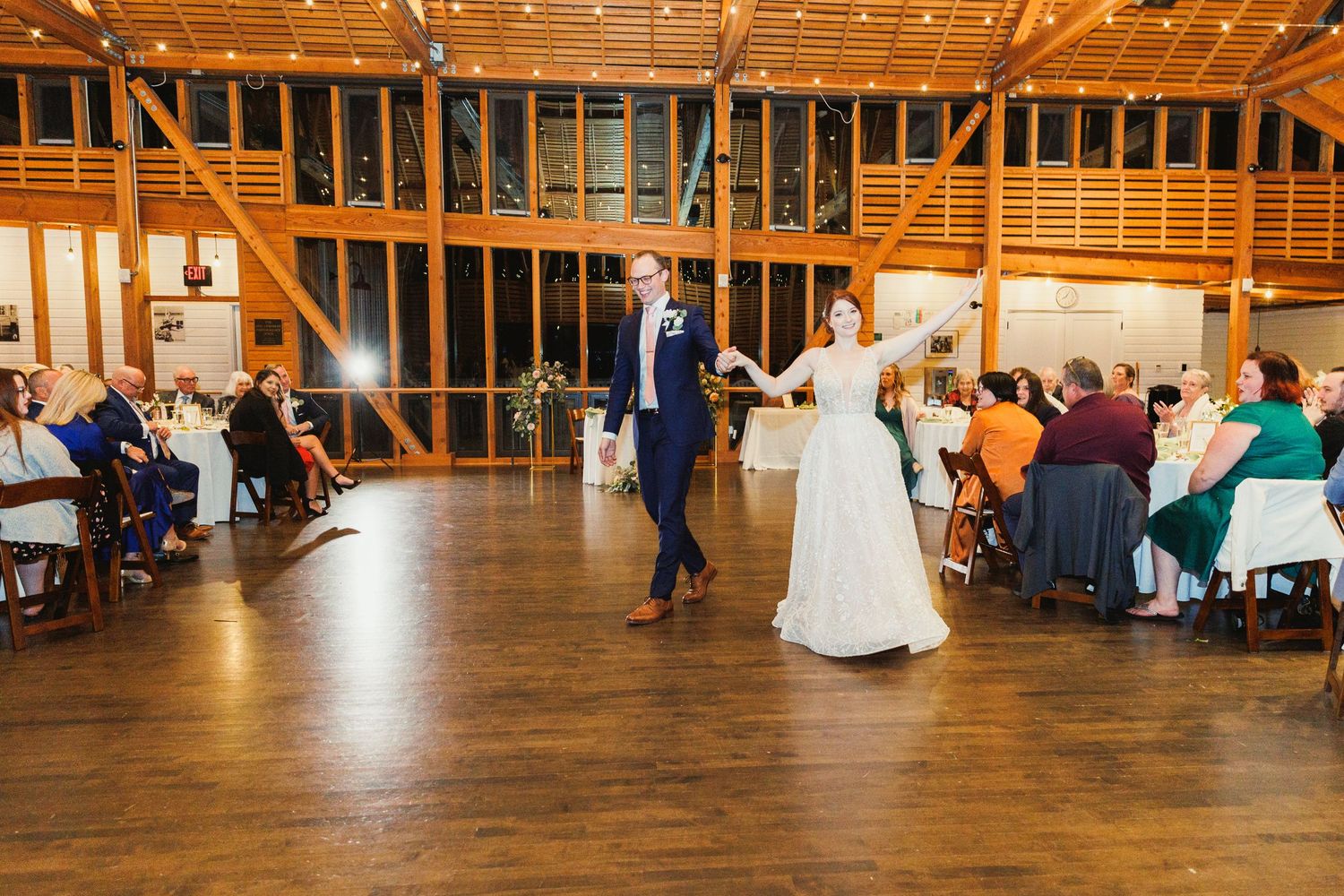Wedding celebration in a rustic wooden barn venue with exposed beams and string lights.