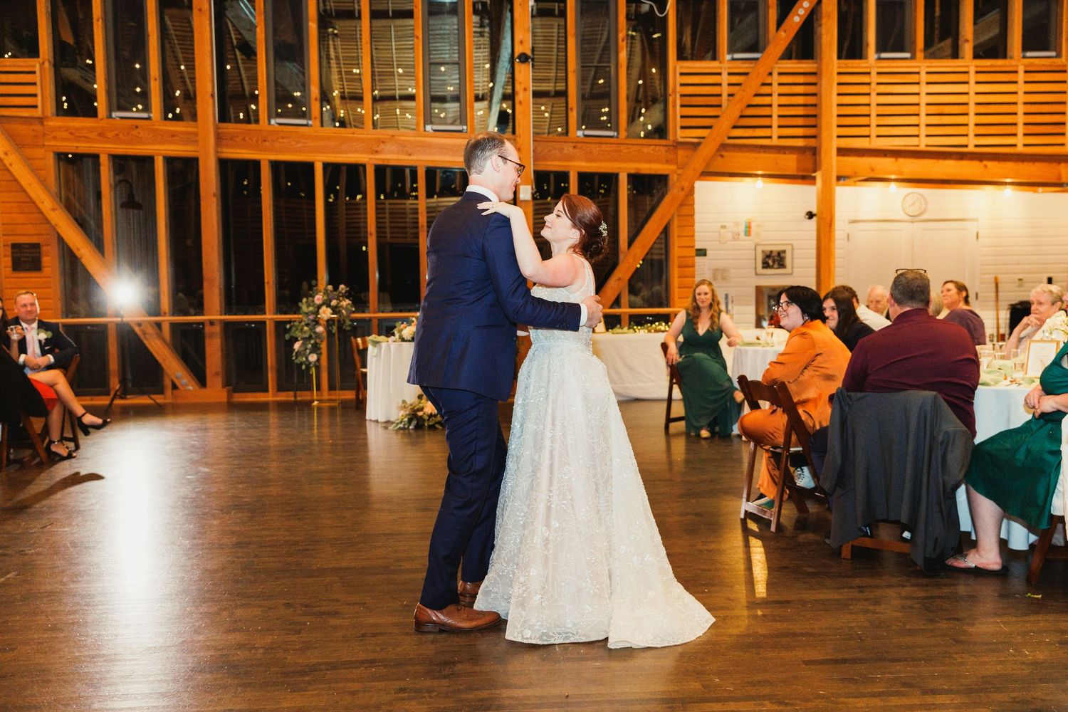 Couple dancing in an elegant barn venue with wooden beams and warm lighting.
