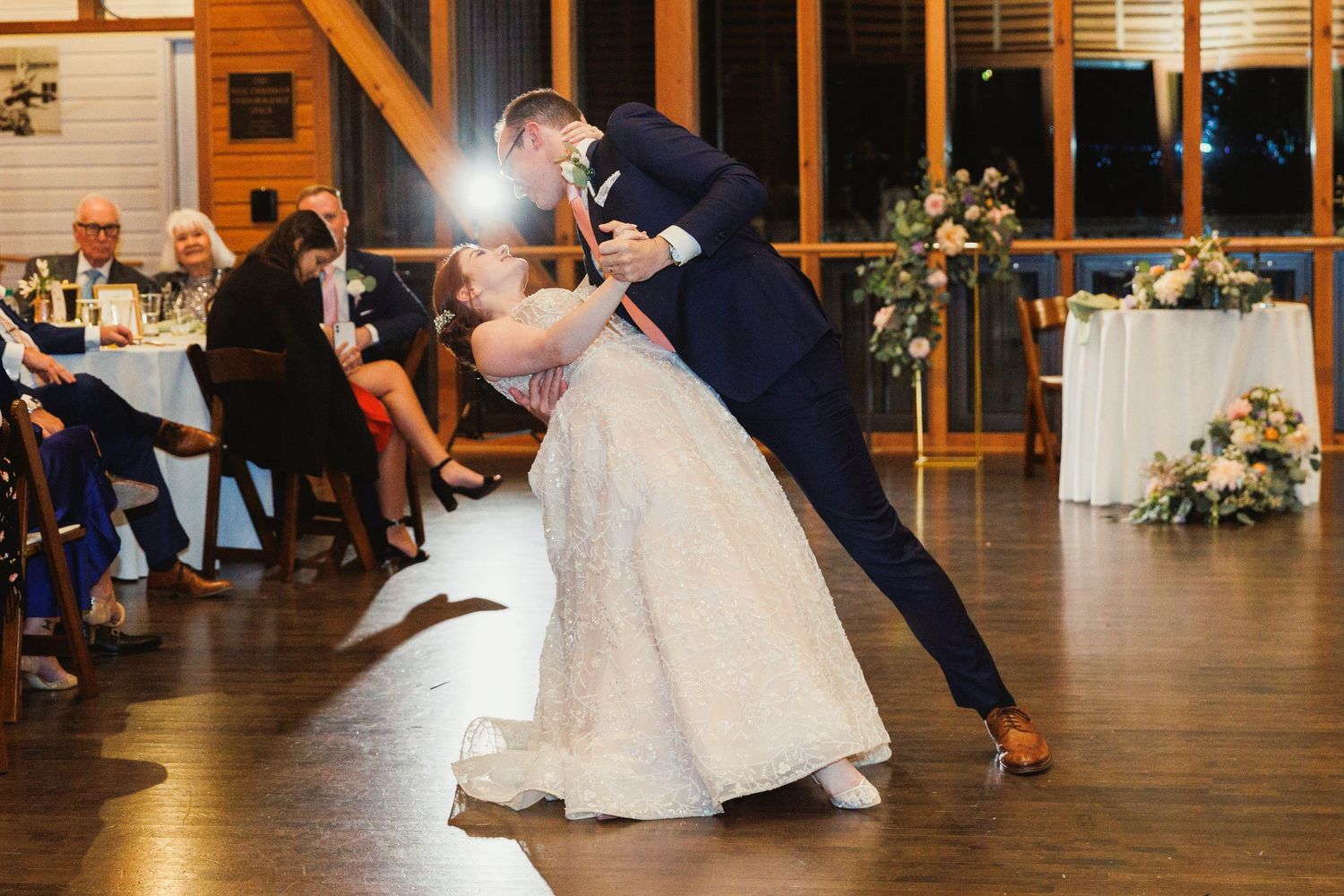 Dramatic dip during wedding dance on wooden floor with guests seated in background.