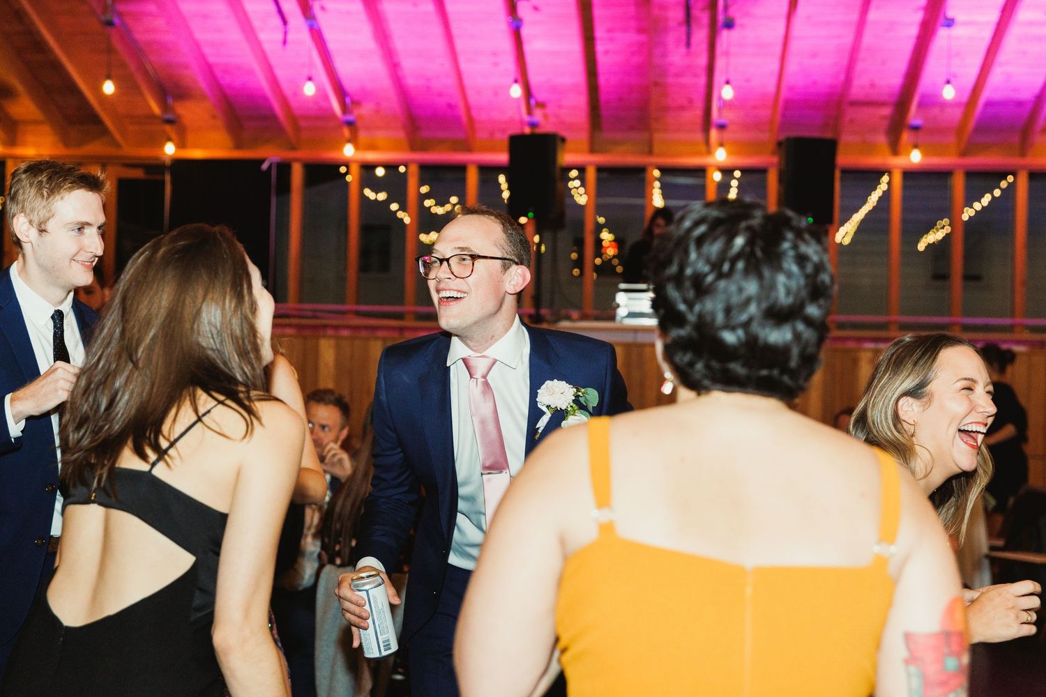 Wedding reception dance party with colorful lighting and guests in formal attire.