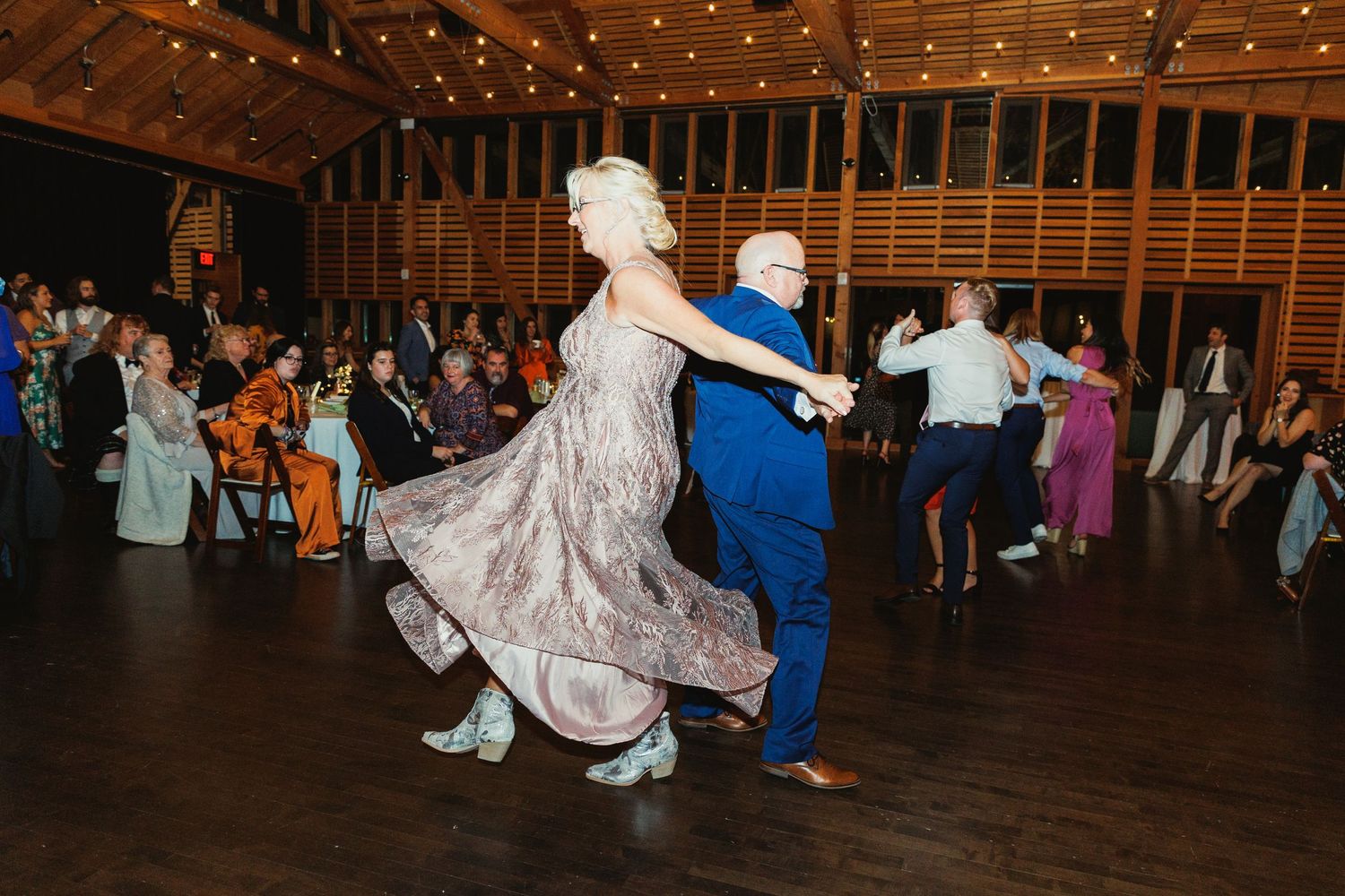 Couples dancing and twirling on a rustic wooden dance floor under twinkling lights.