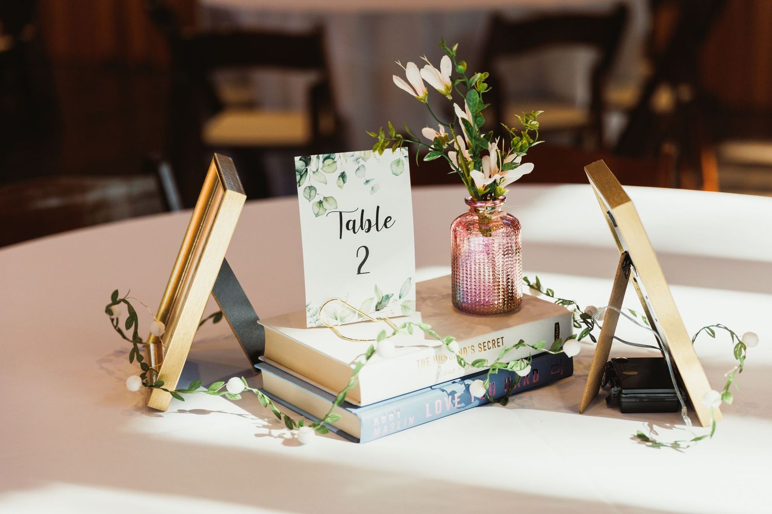Vintage book centerpiece with table number card and pink glass vase on white tablecloth.