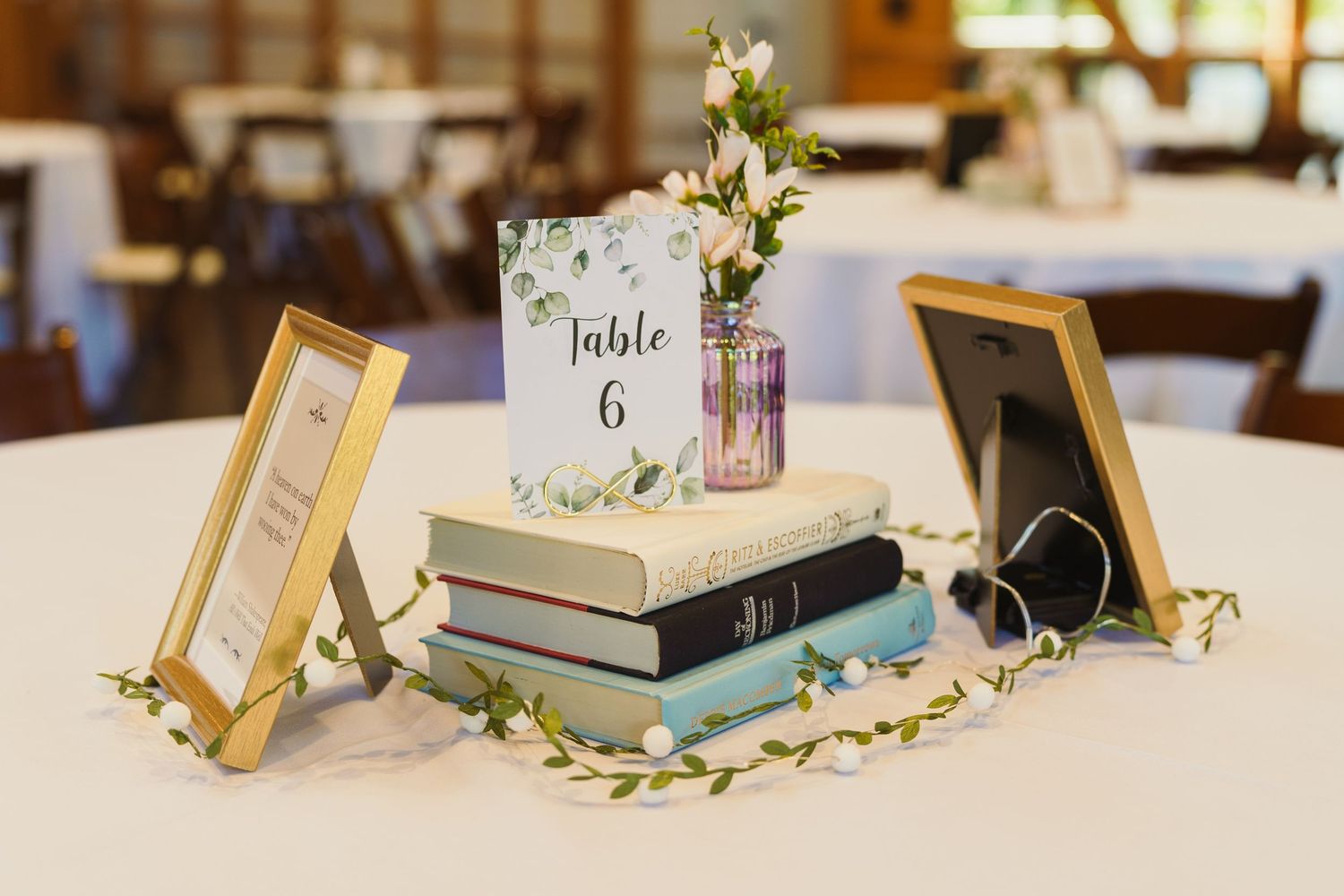 Wedding table centerpiece featuring books, table number, and delicate floral accents.