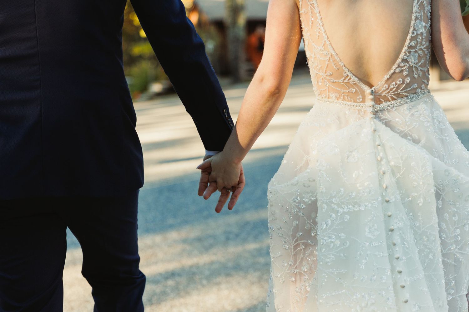 Close-up of couple holding hands while walking in elegant wedding attire.