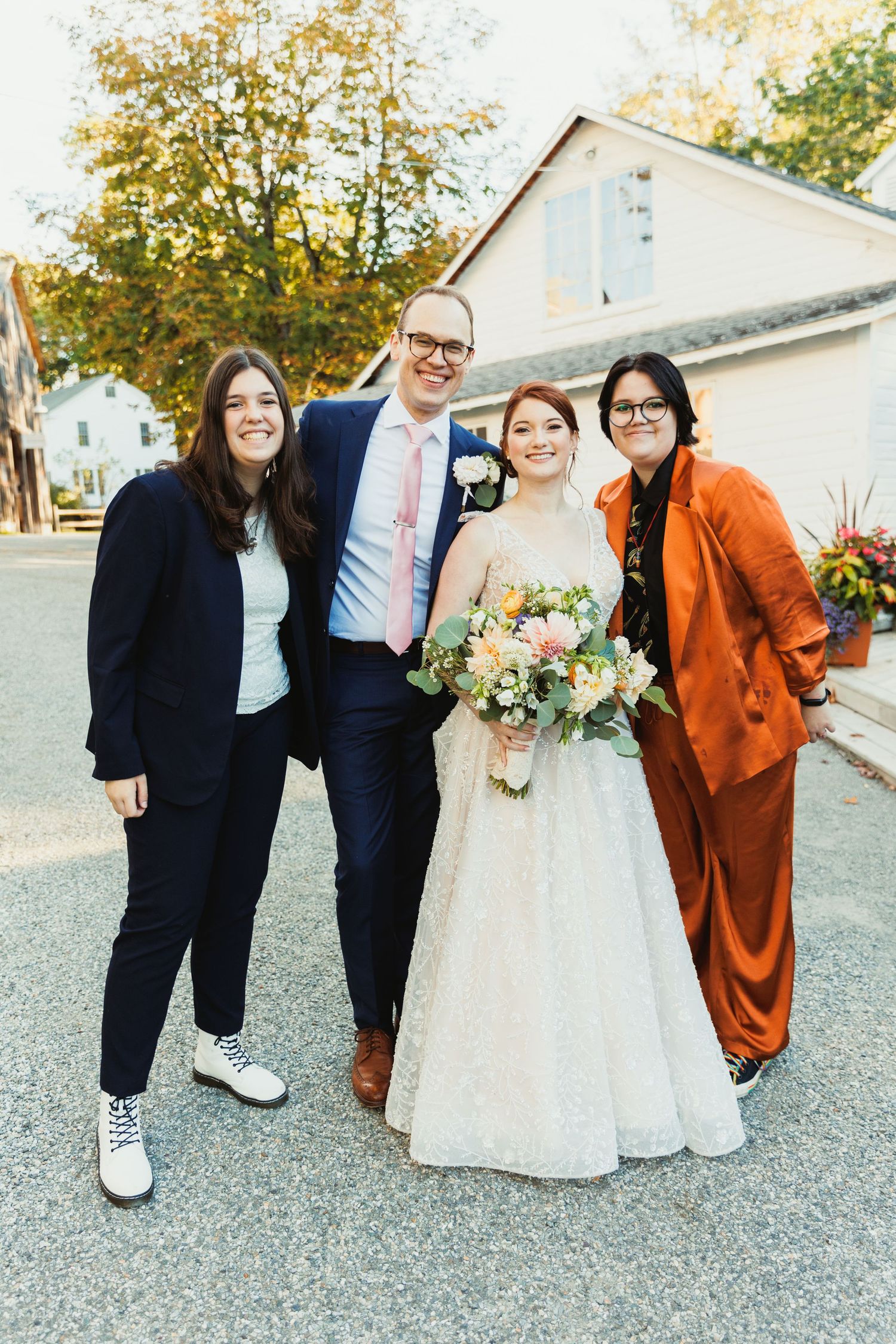 Wedding party poses outdoors in autumn with bride in white dress and attendants in orange and navy blue attire.
