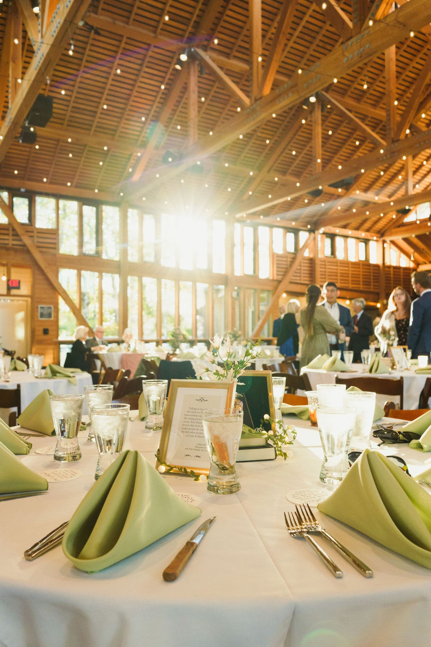 Elegant table settings in rustic barn venue with green napkins and warm lighting.