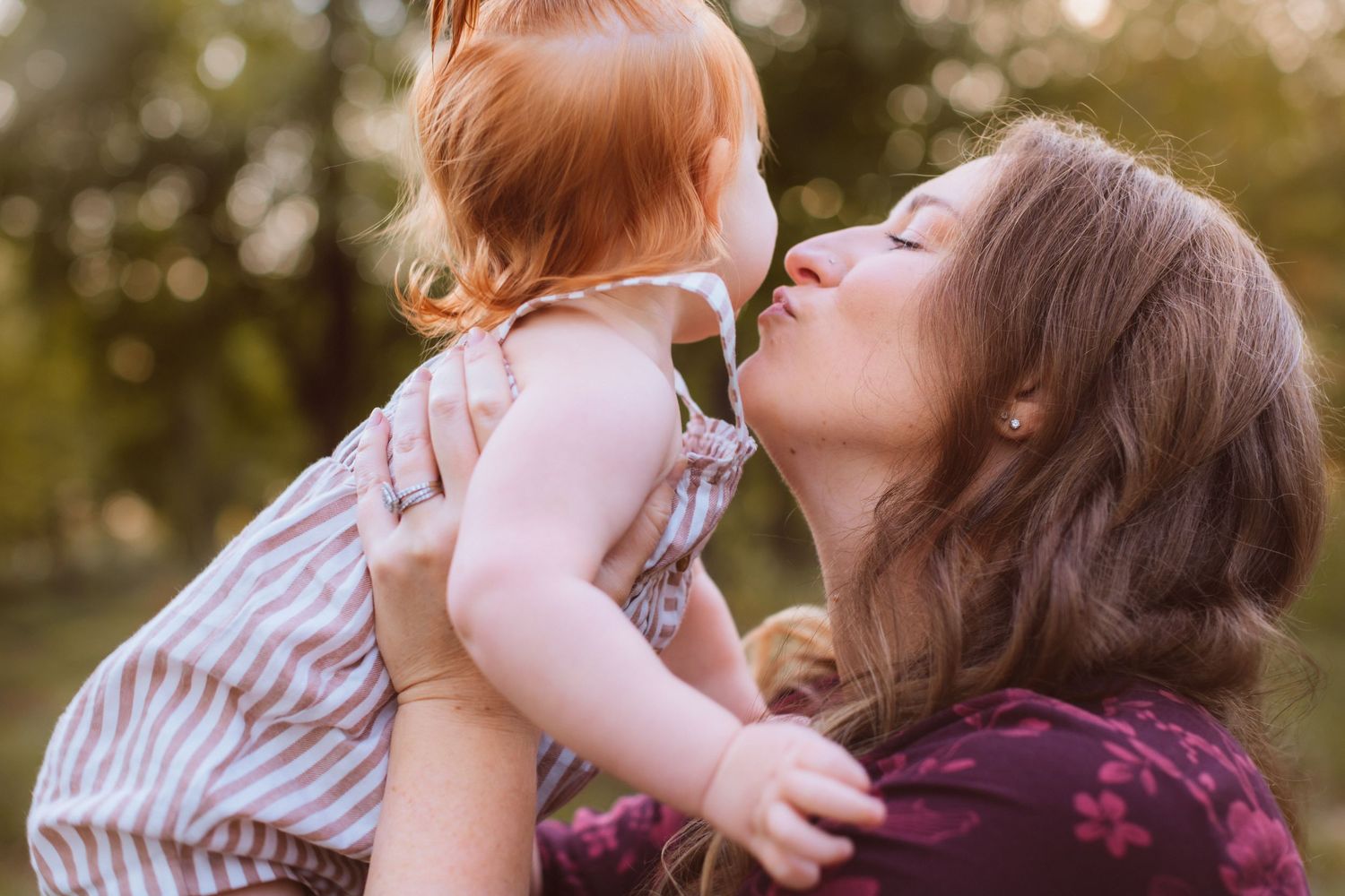A proud mom holds up her adorable baby girl and kisses her on the cheek.