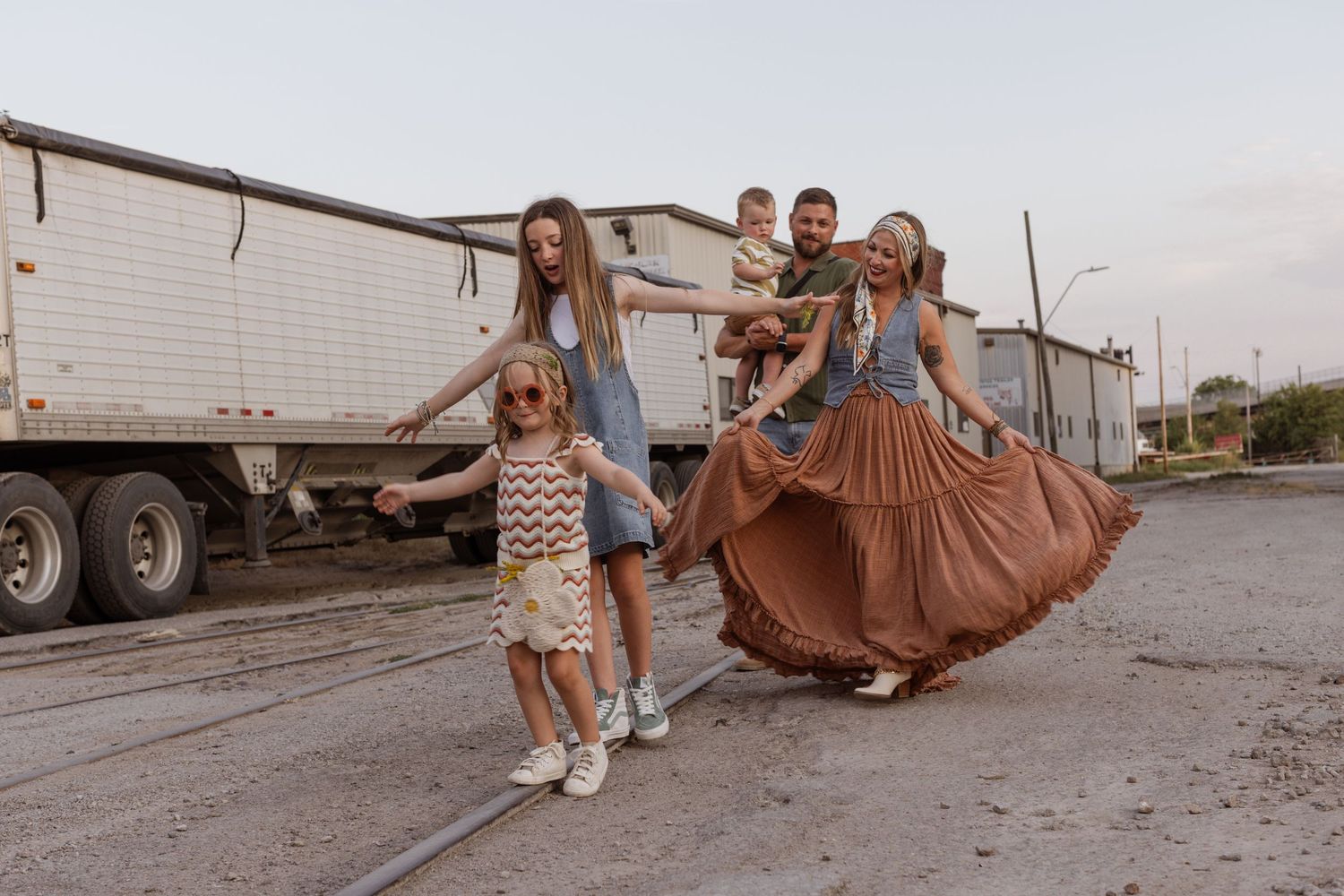 A boho-styled family of five walks along abandoned train tracks in a gritty urban scene.