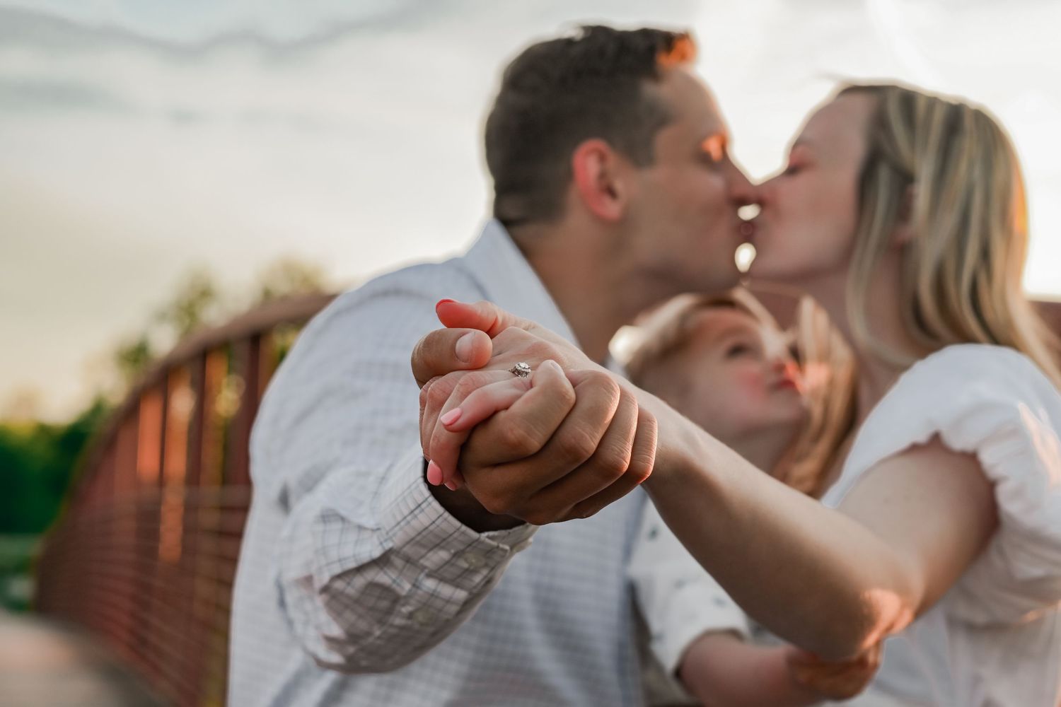 A romantic couple shares a tender kiss while holding hands at sunset on a brick-lined path.