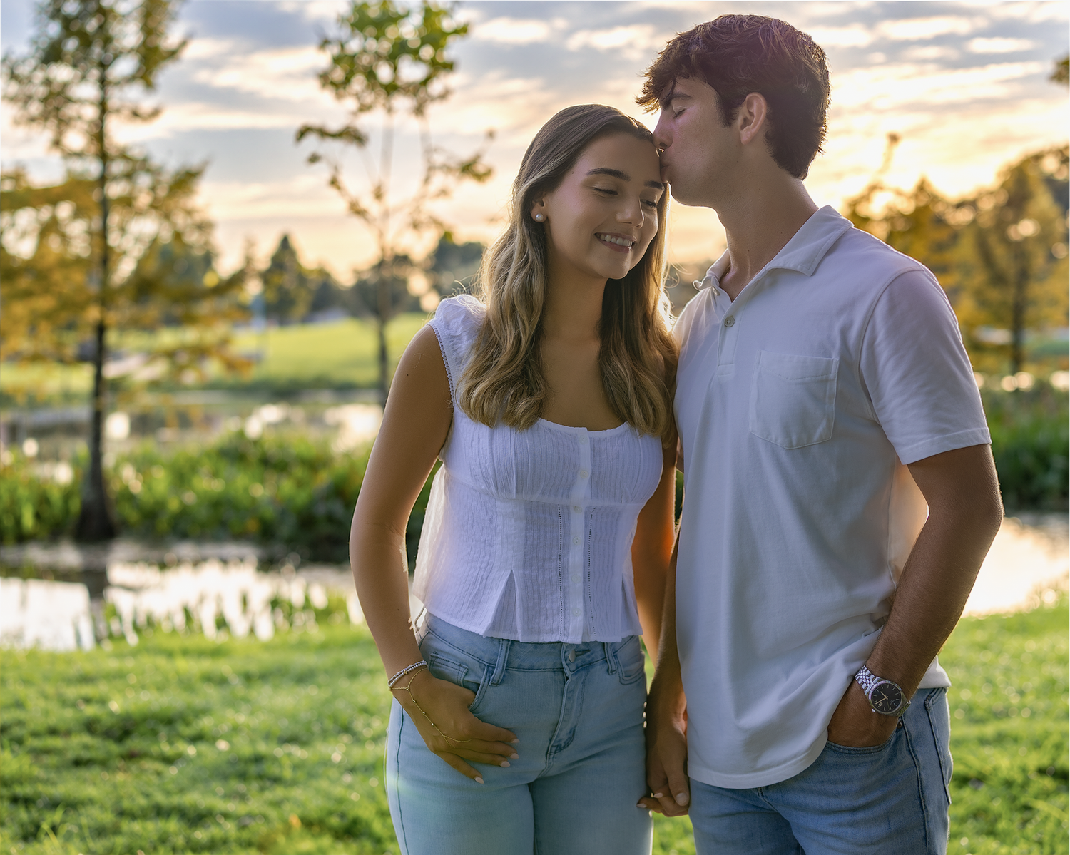 Young couple sharing a romantic moment at sunset in a lush green park near a pond.