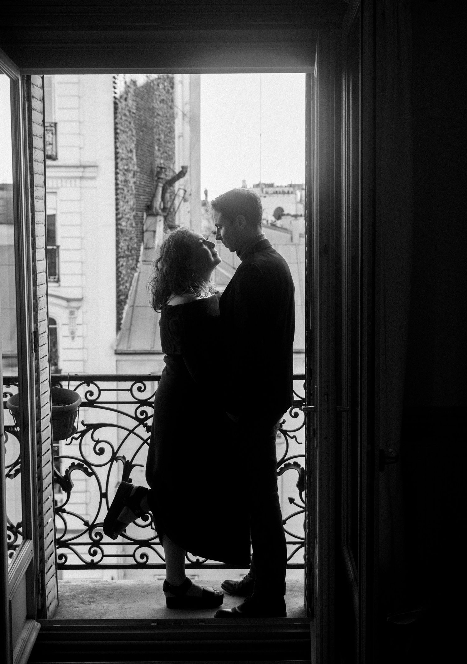 A romantic silhouette of a couple embracing on a Parisian balcony with ornate iron railings.
