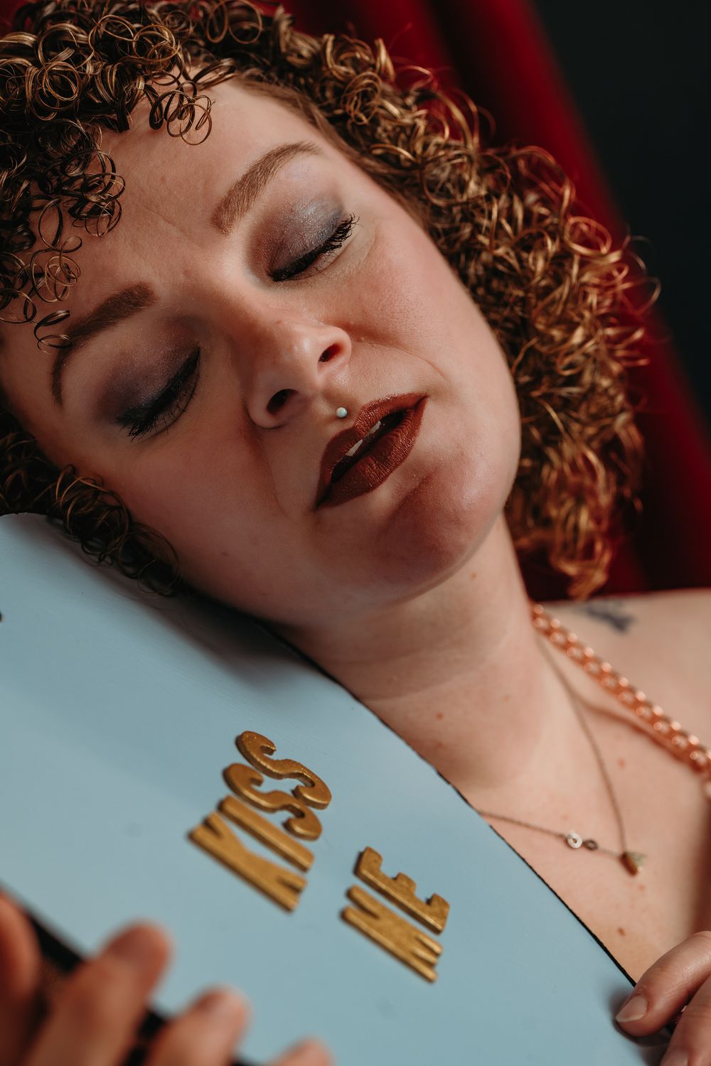 Artistic portrait with curly hair and pearl necklace against a light blue background.