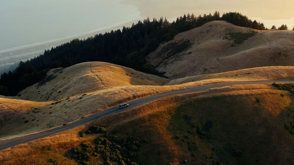Winding mountain road along golden hills during sunset in California.