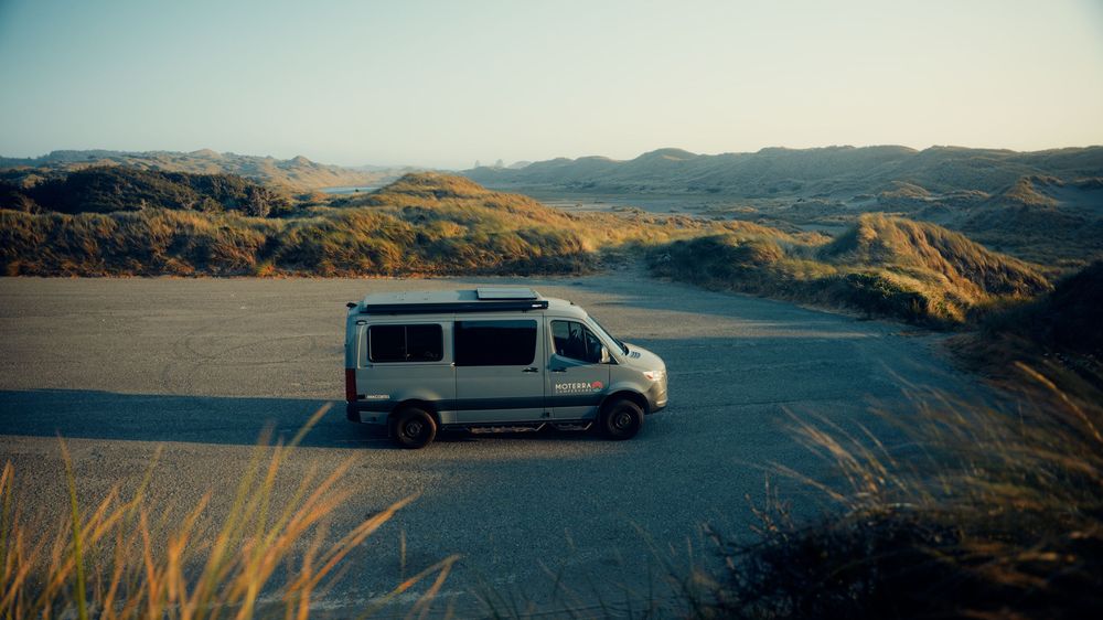 Mountain landscape with a parked van overlooking a vast valley during golden hour.