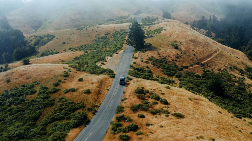 Aerial view of a lone vehicle on winding mountain road through golden hills.