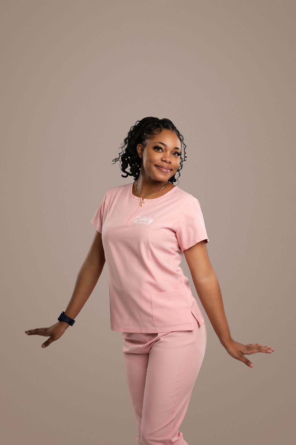 Professional model wearing pink scrubs poses playfully against neutral background.