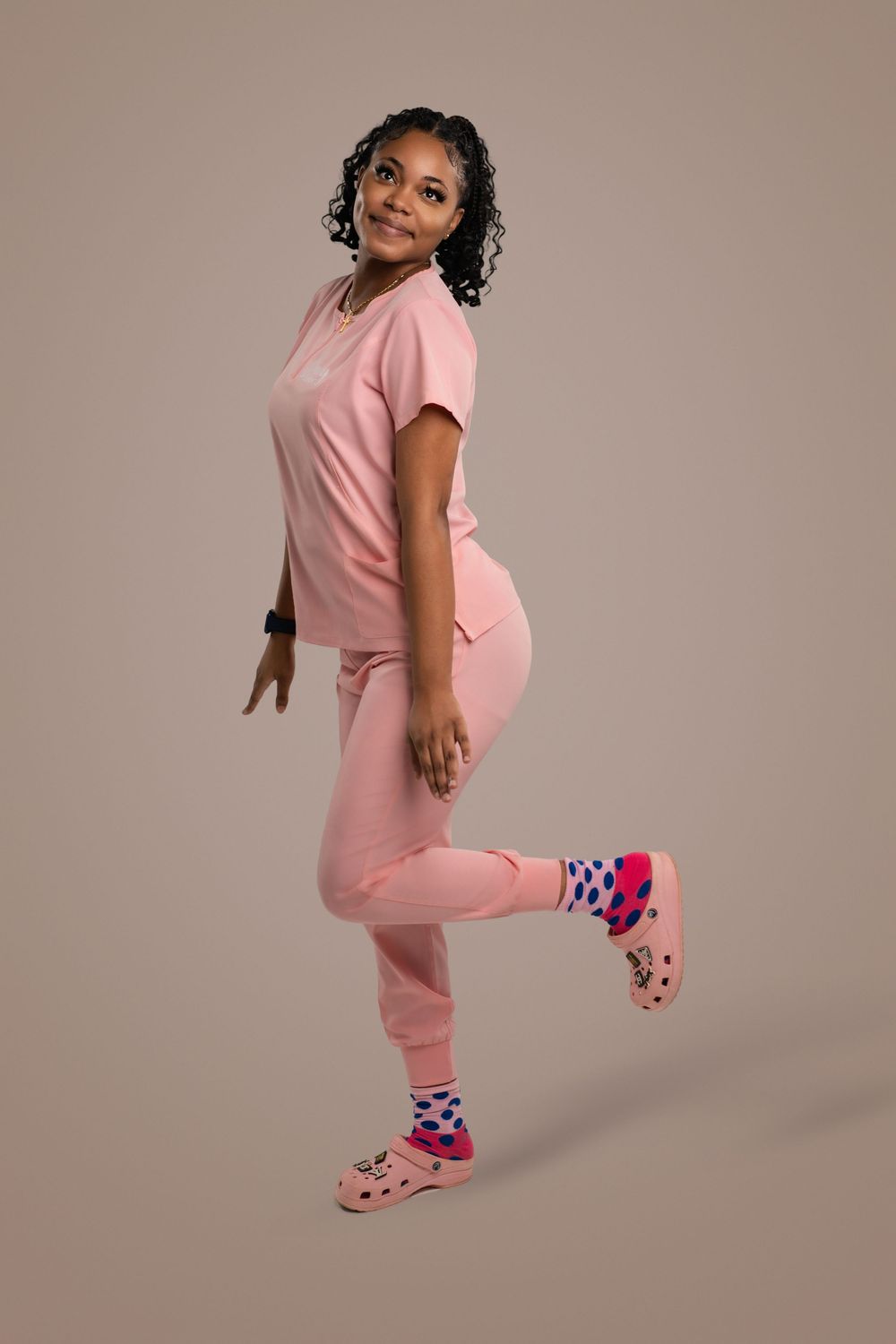 A person wearing pink scrubs and colorful checkered socks poses in various playful positions against a neutral backdrop.