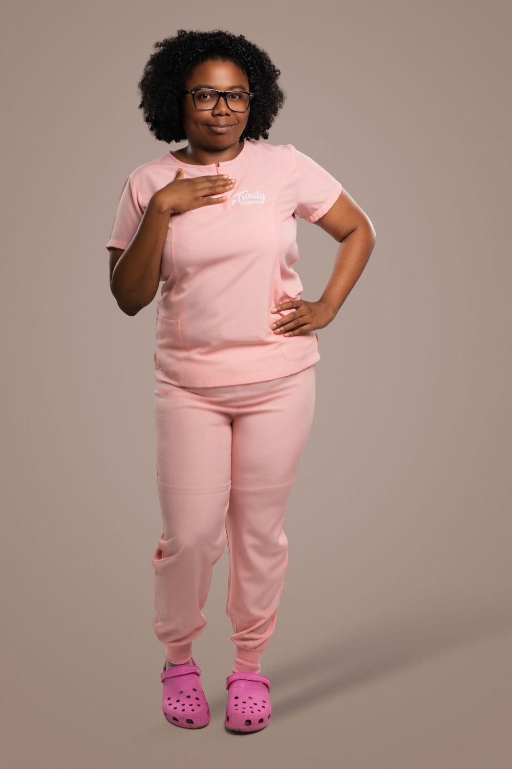 A person wearing a pink matching loungewear set and pink crocs poses confidently against a gray backdrop.