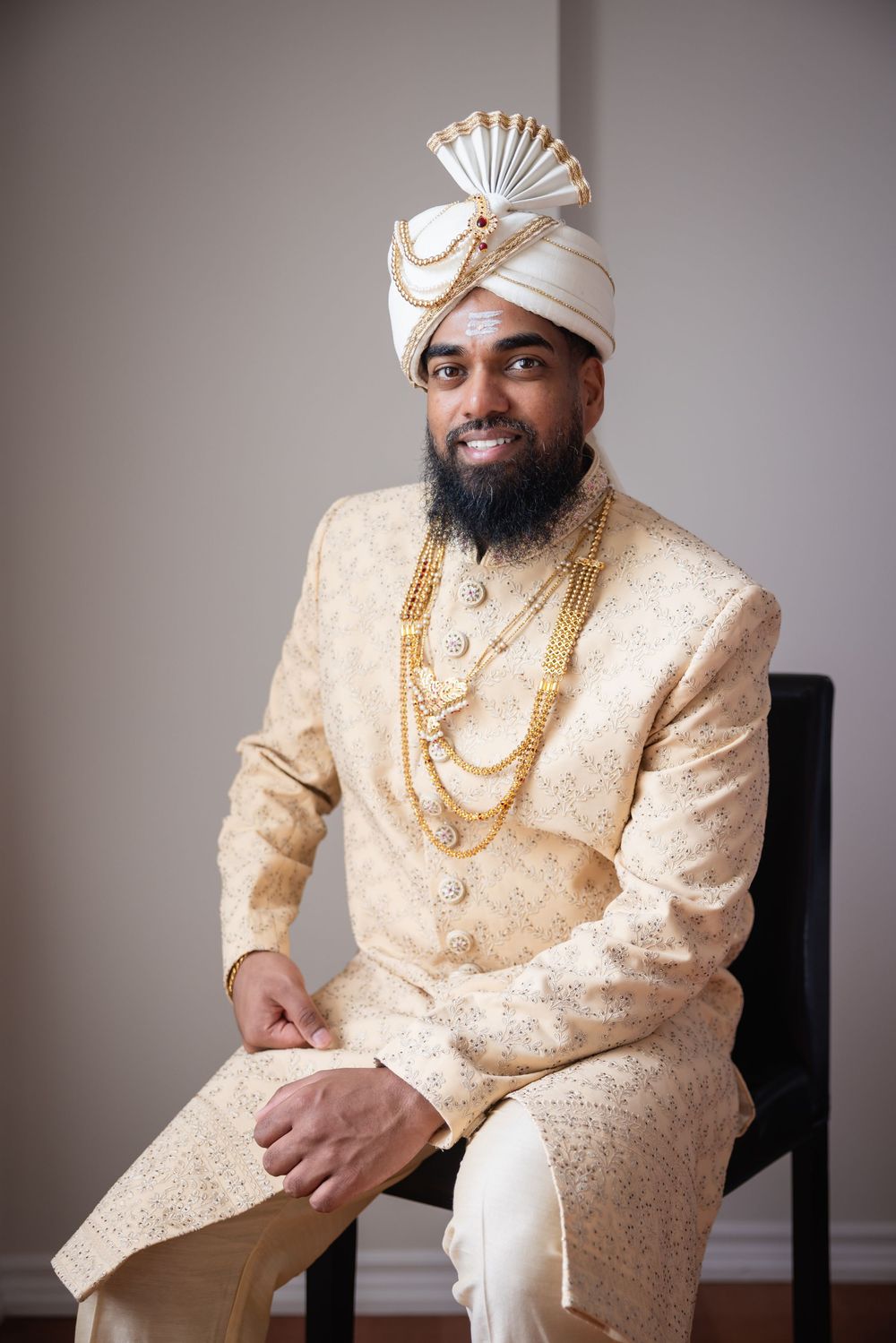 A person in a cream-colored traditional Indian wedding sherwani with gold embellishments poses for formal portraits.