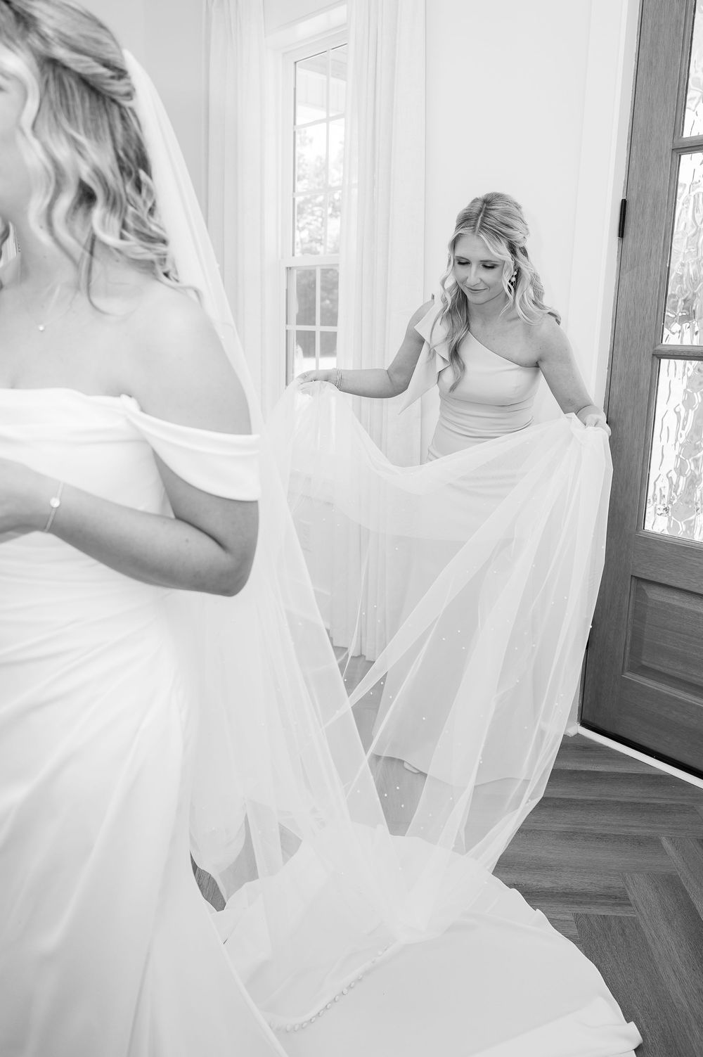 Black and white photo of wedding dress details being arranged on herringbone floors.