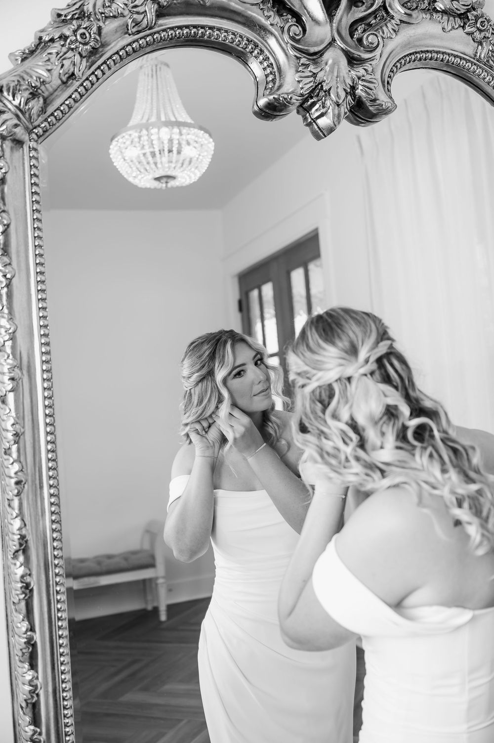 Reflection in ornate mirror shows wedding preparation moment under crystal chandelier.