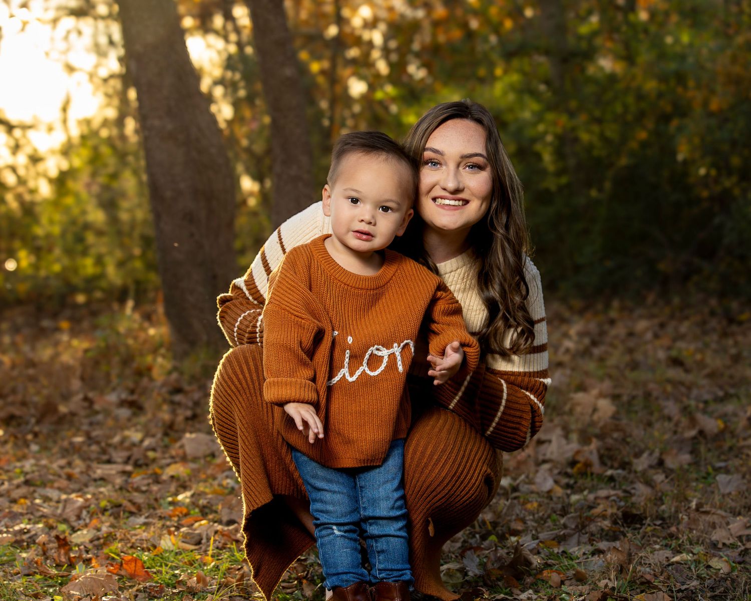 A mother and child in brown sweaters share playful moments together during an autumn outdoor photoshoot.