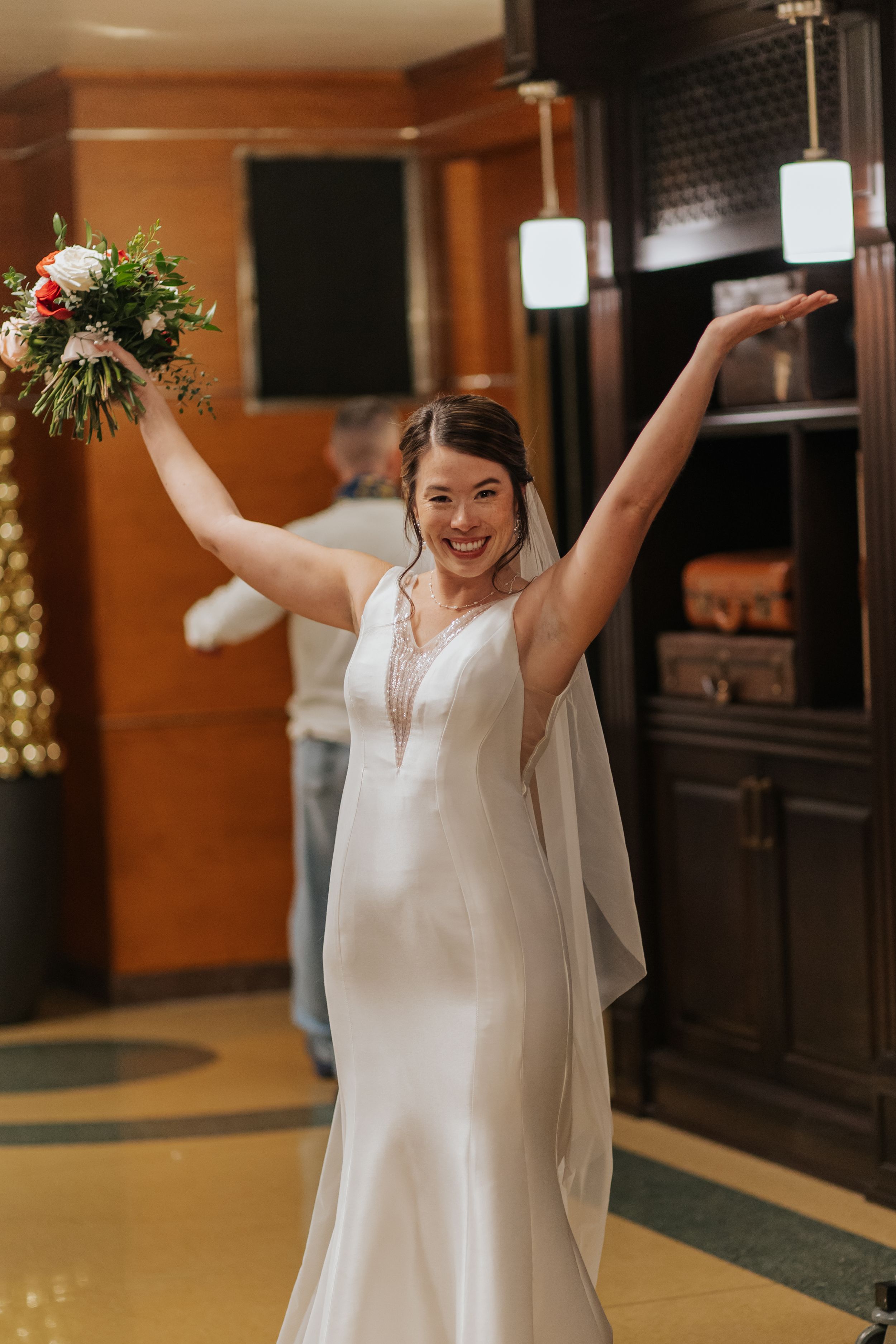 A bride in a white dress joyfully celebrates at an indoor venue with warm lighting.