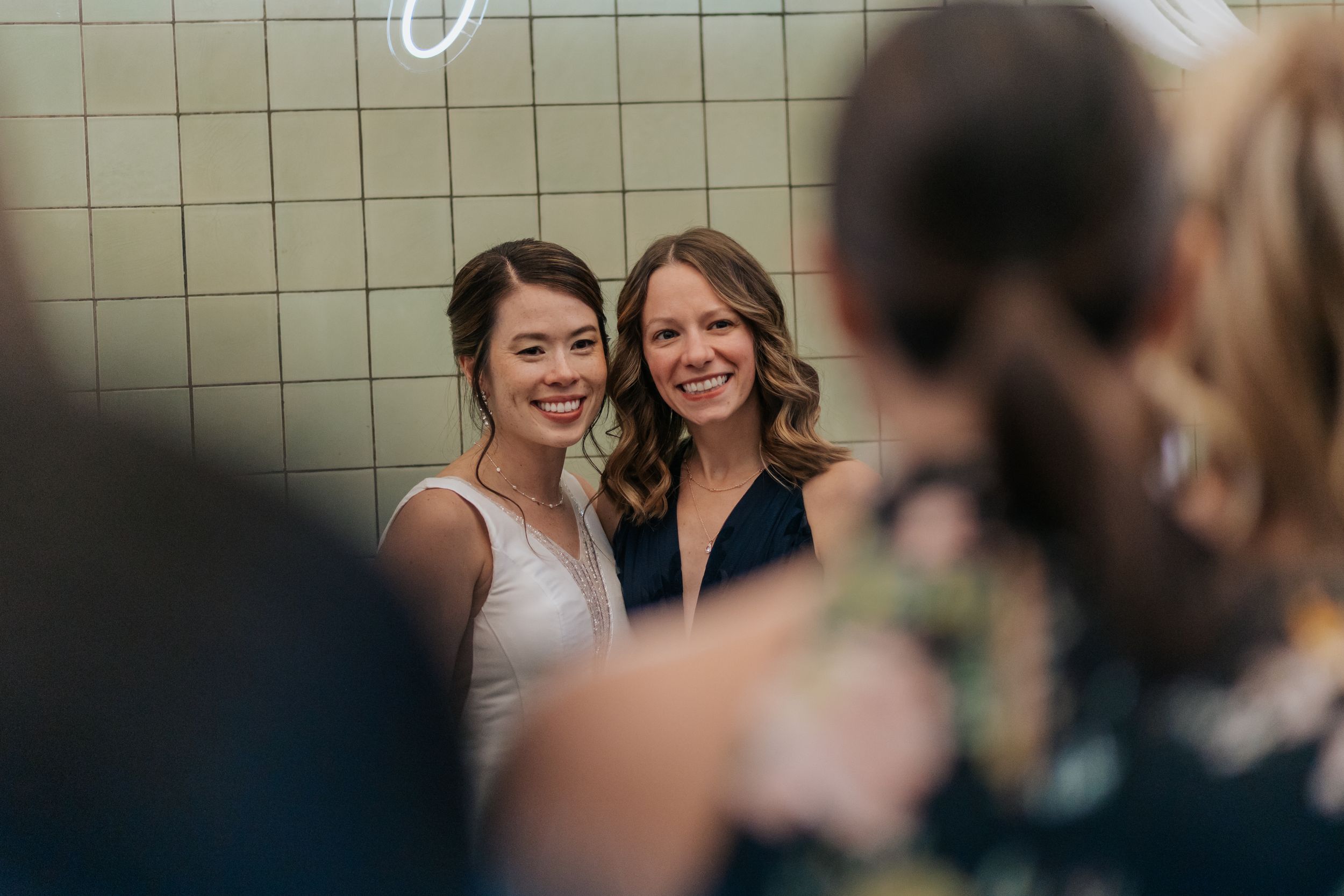 Bride and bridesmaids share a joyful moment together while standing behind a mesh fence at an outdoor wedding.