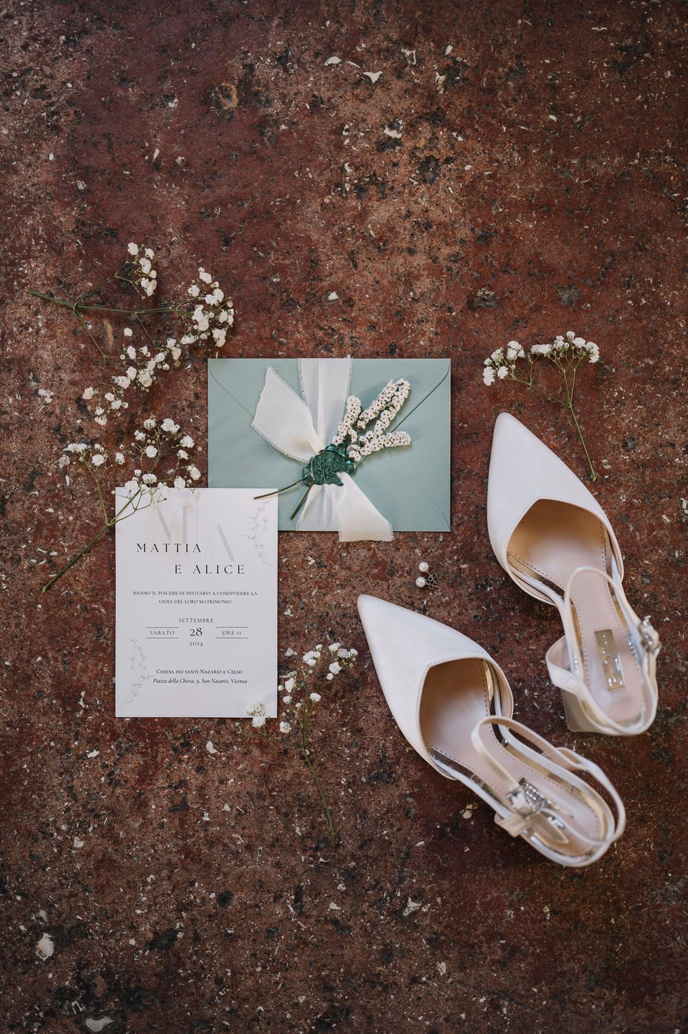 Wedding invitation and white heels arranged on rustic textured surface.