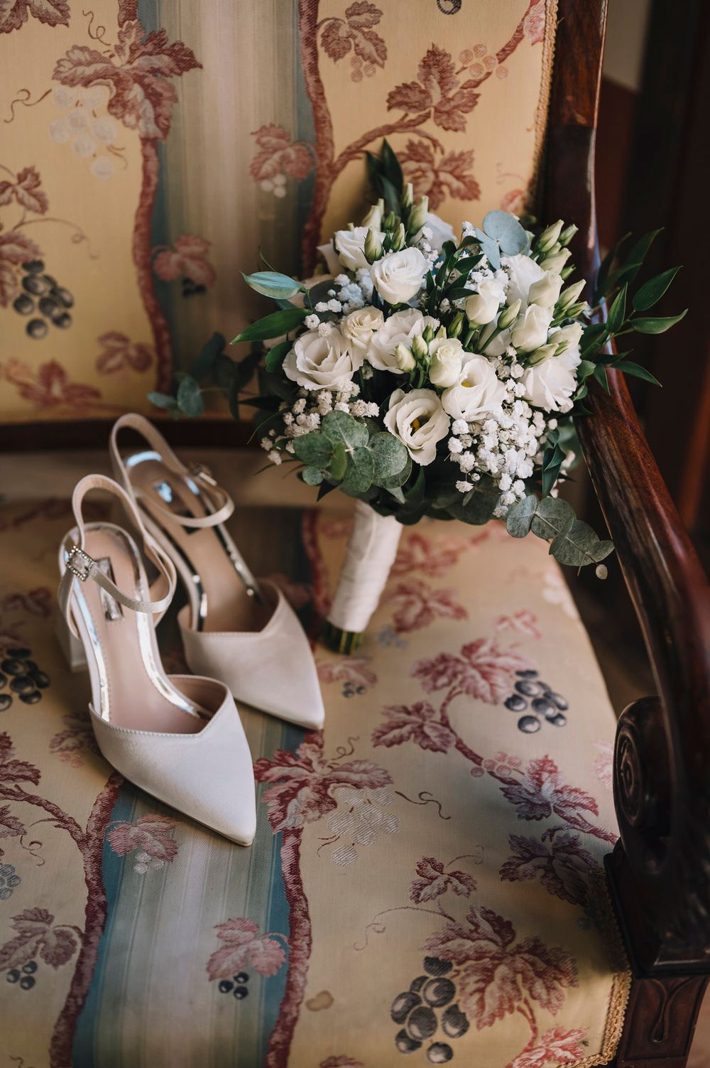 Elegant white bridal shoes with floral arrangements on a vintage patterned background.