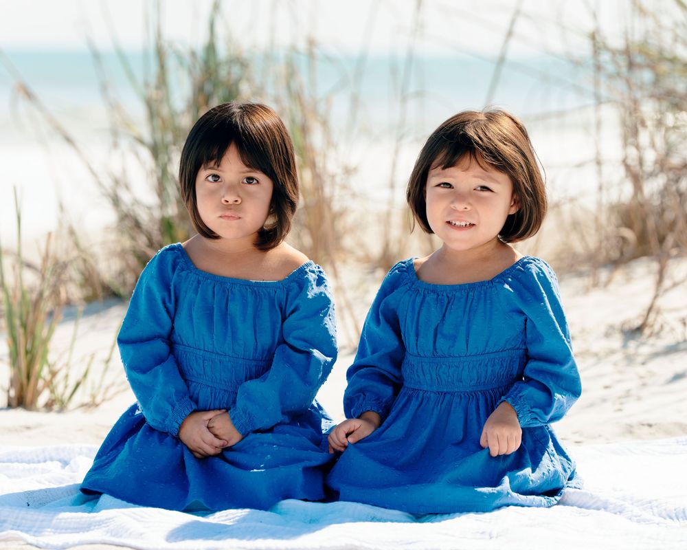 Two children in matching bright blue dresses pose together on a sandy beach during winter.