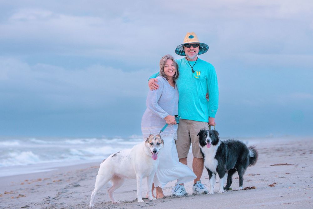 Group enjoying a casual stroll along the shoreline with their white dog on a cloudy beach day.