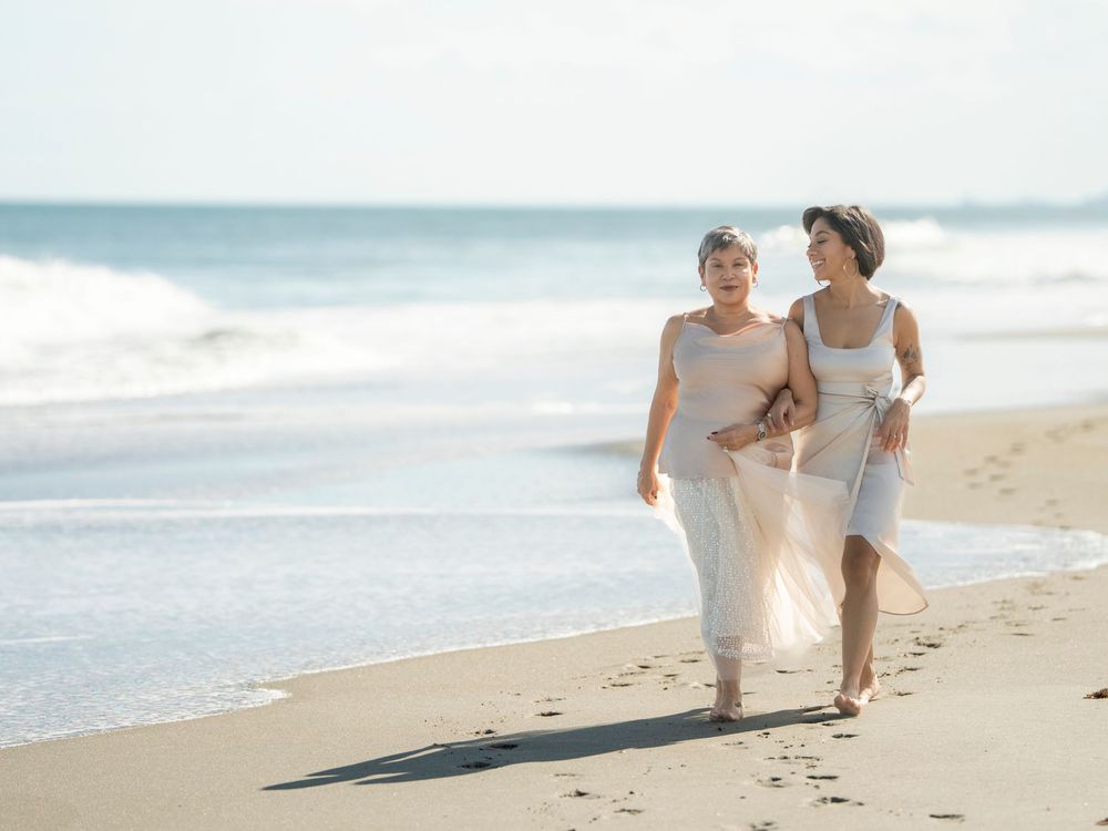 Two people walking together on sandy beach leaving footprints near ocean waves at sunset.