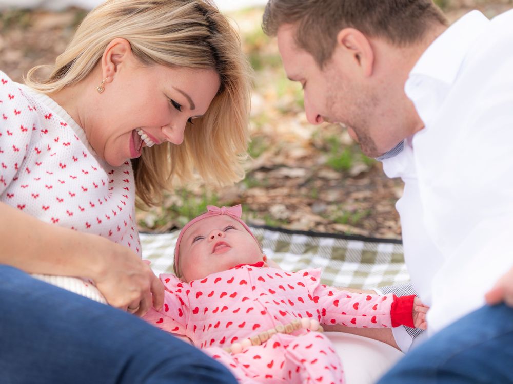 A loving couple shares tender moments with their baby while sitting outdoors on a blanket during a family photo session.