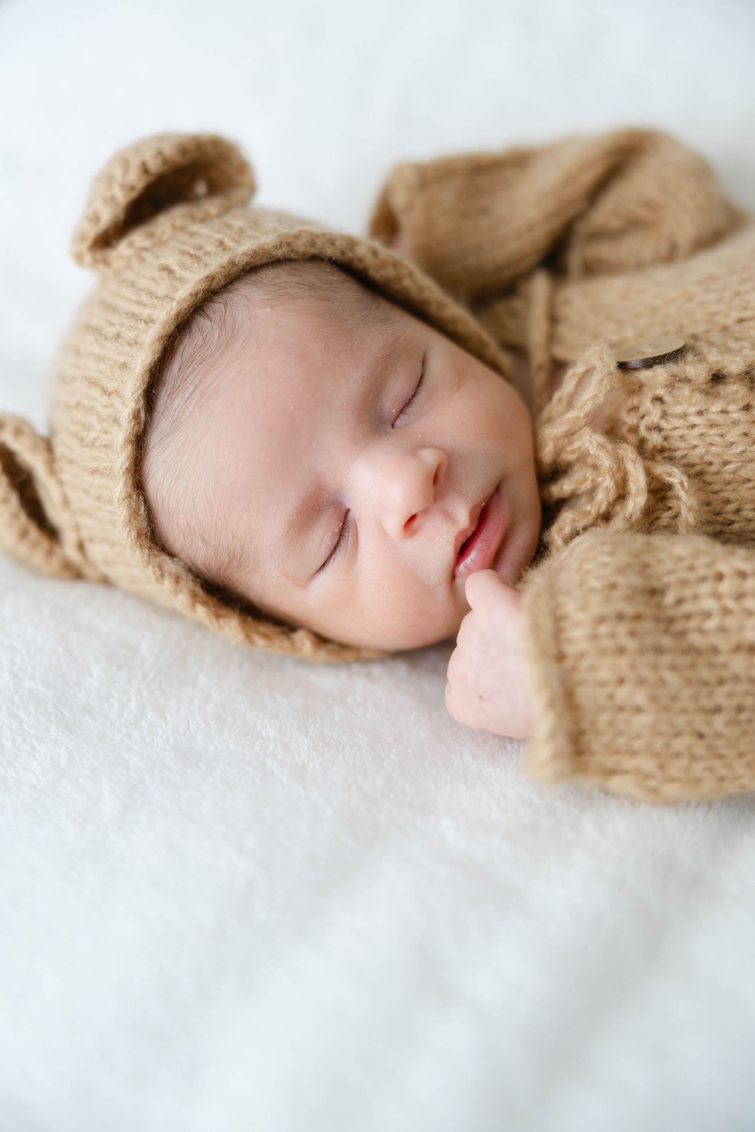 Sleeping newborn baby wearing a knit bonnet and wrapped in a neutral blanket during a lifestyle newborn session.