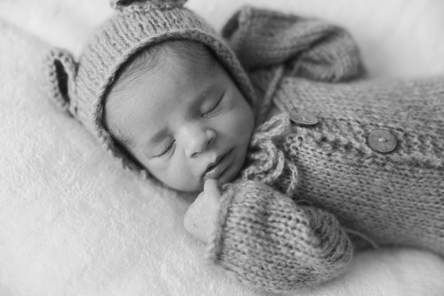 Black and white photo of a sleeping newborn baby wrapped in soft knit layers during a lifestyle newborn session.