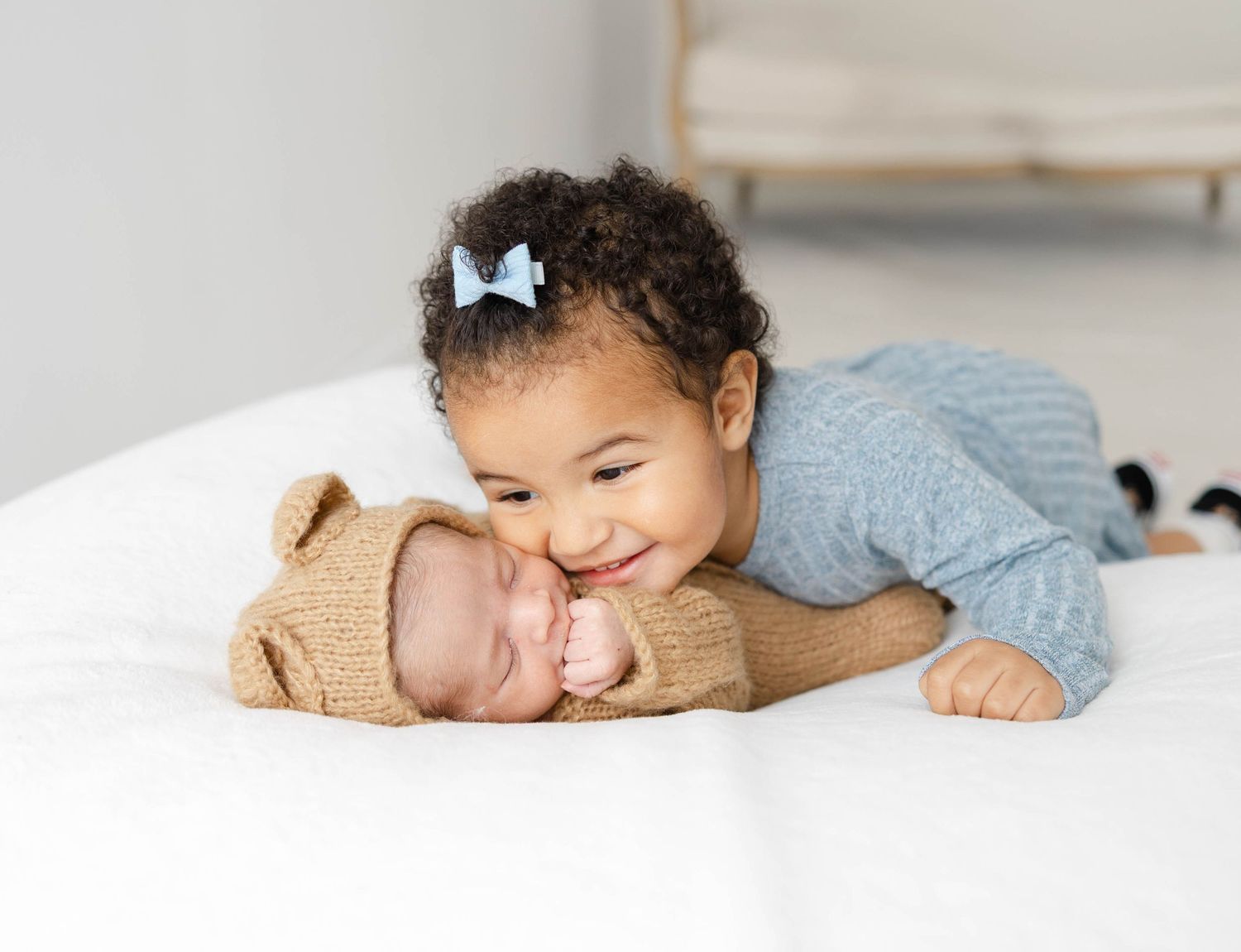 Sibling gently kissing a newborn baby on the bed during a heartfelt lifestyle family photography session.