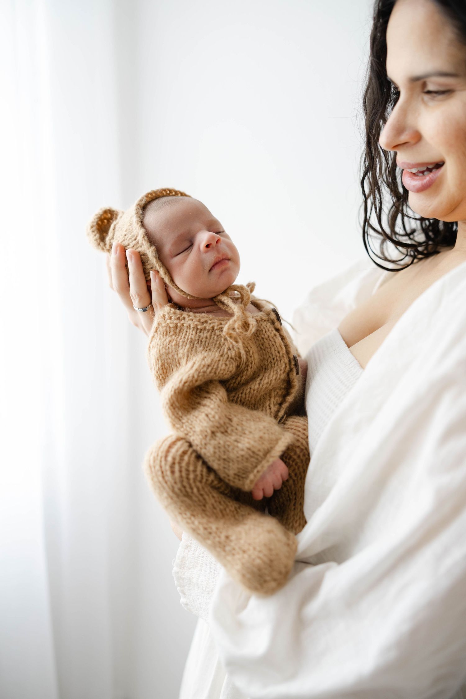 Mother holding her newborn baby near a window in soft natural light during a lifestyle newborn session.