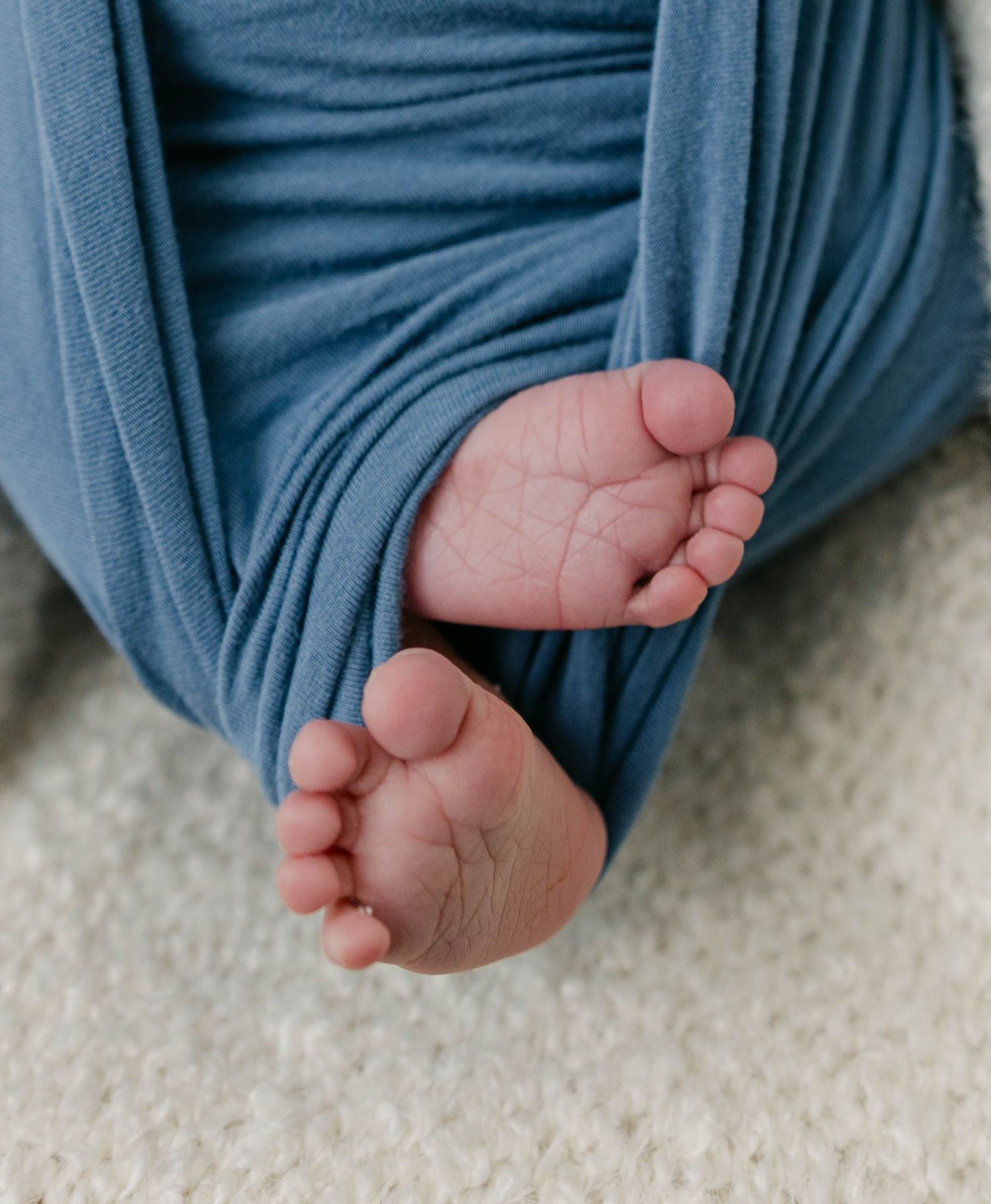 Close-up detail photo of a newborn baby’s feet wrapped in soft fabric during a lifestyle newborn session.