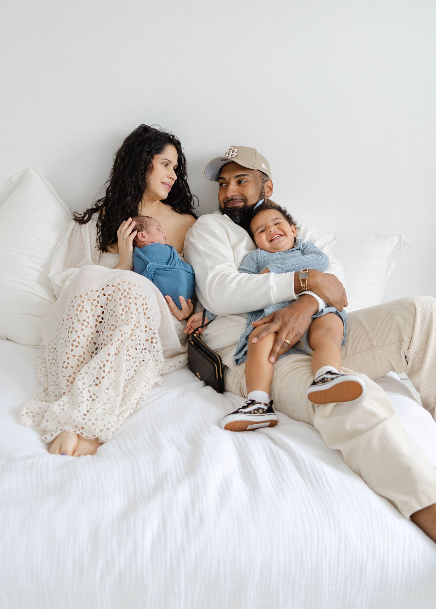 Parents sitting together on a bed holding their newborn baby during a relaxed in-home lifestyle session.
