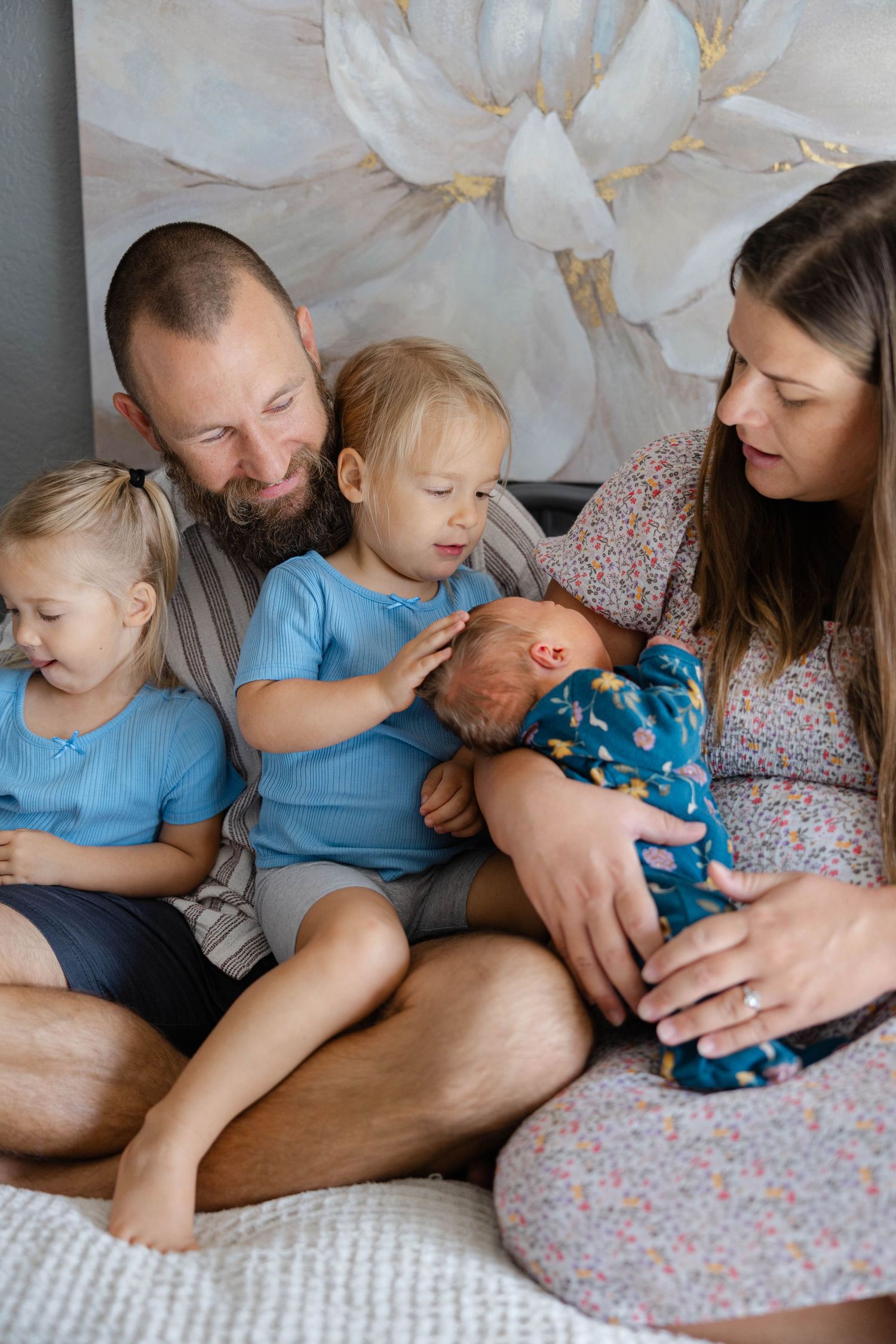 Lifestyle newborn session with parents and toddlers sitting together on a bed while holding their newborn baby.