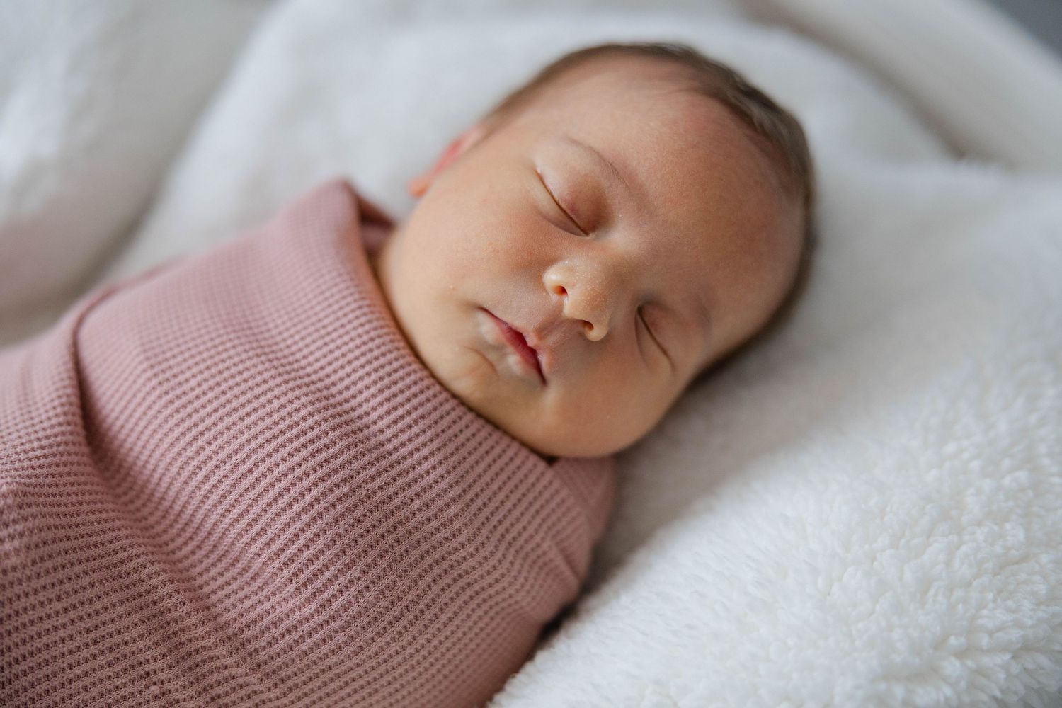 Sleeping newborn baby swaddled in a neutral wrap during an in-home lifestyle newborn photography session.
