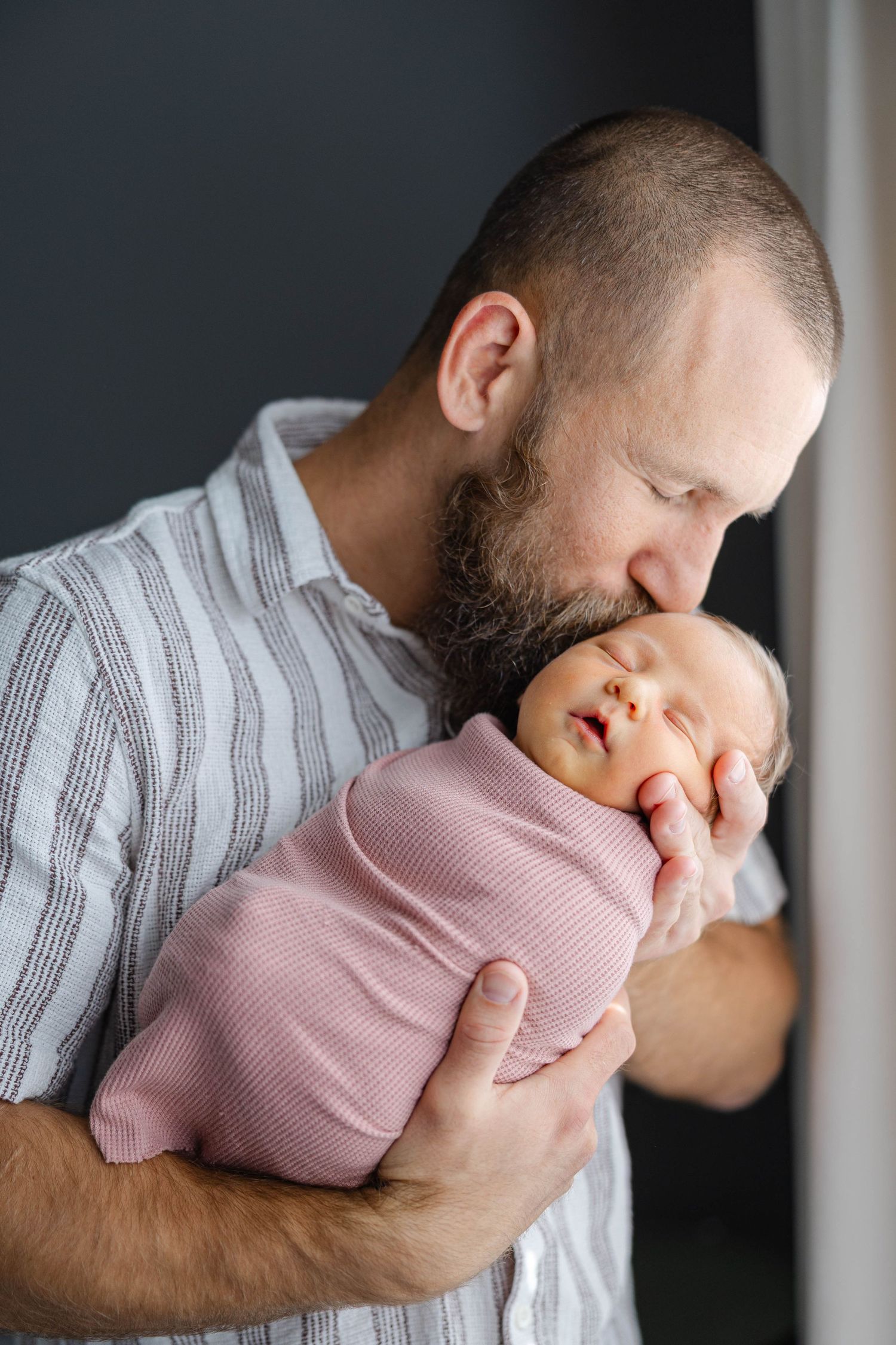 Father holding his newborn baby close during a lifestyle newborn photography session in soft natural light.