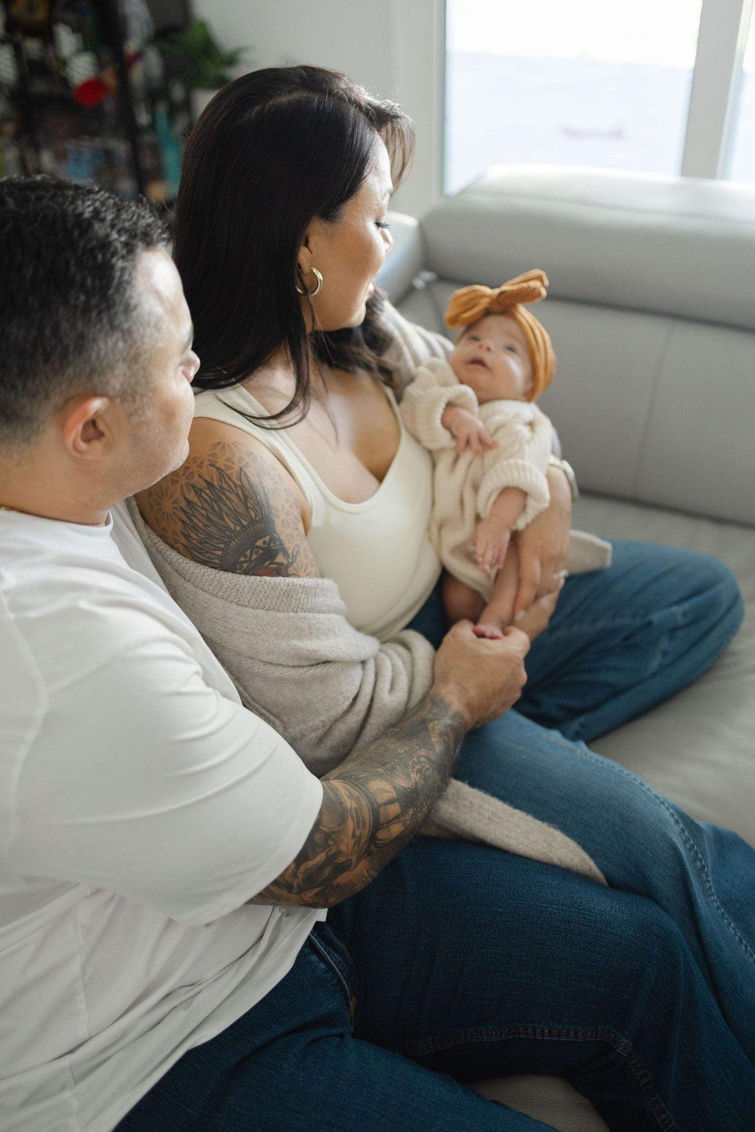 Parents sitting together on a bed holding their newborn baby during a relaxed in-home lifestyle session.