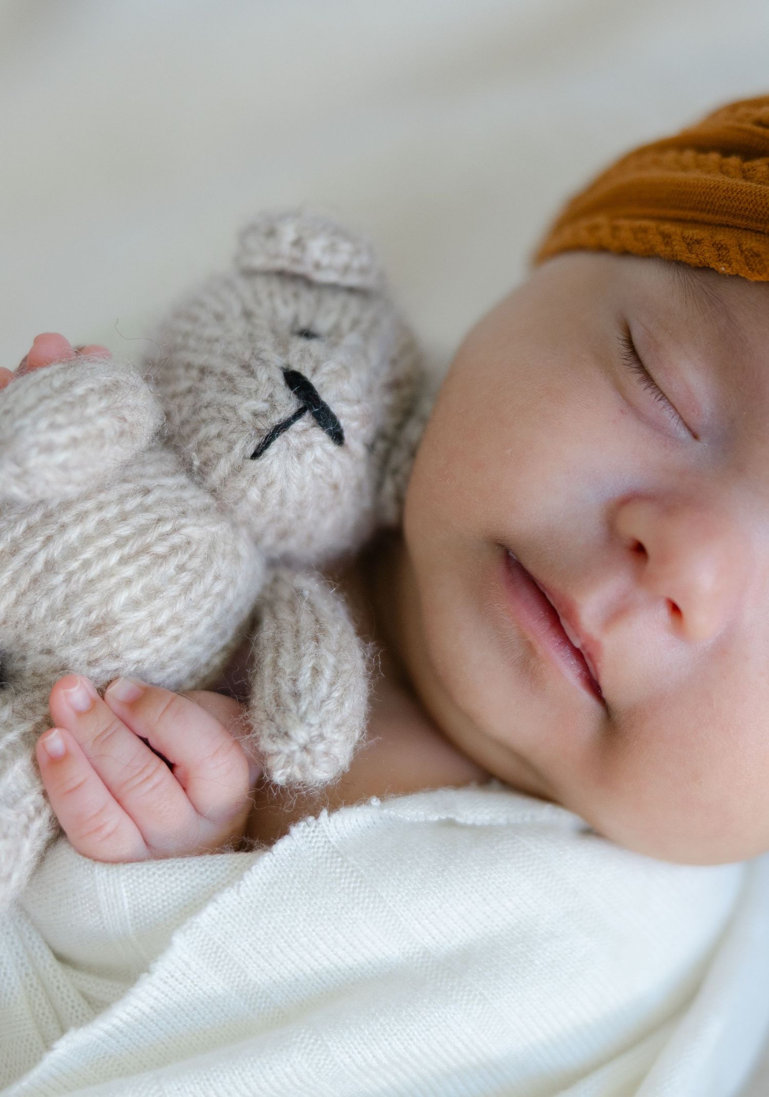Lifestyle family session featuring parents sitting on a bed with their newborn baby in a relaxed, light-filled space.