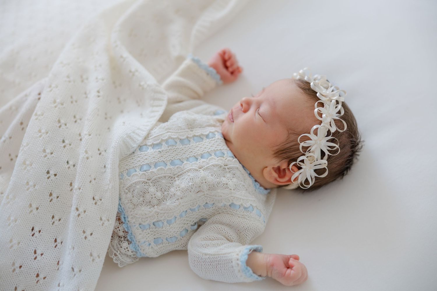 Sleeping newborn baby wearing a delicate headband and wrapped in a soft blanket during a lifestyle photography session.